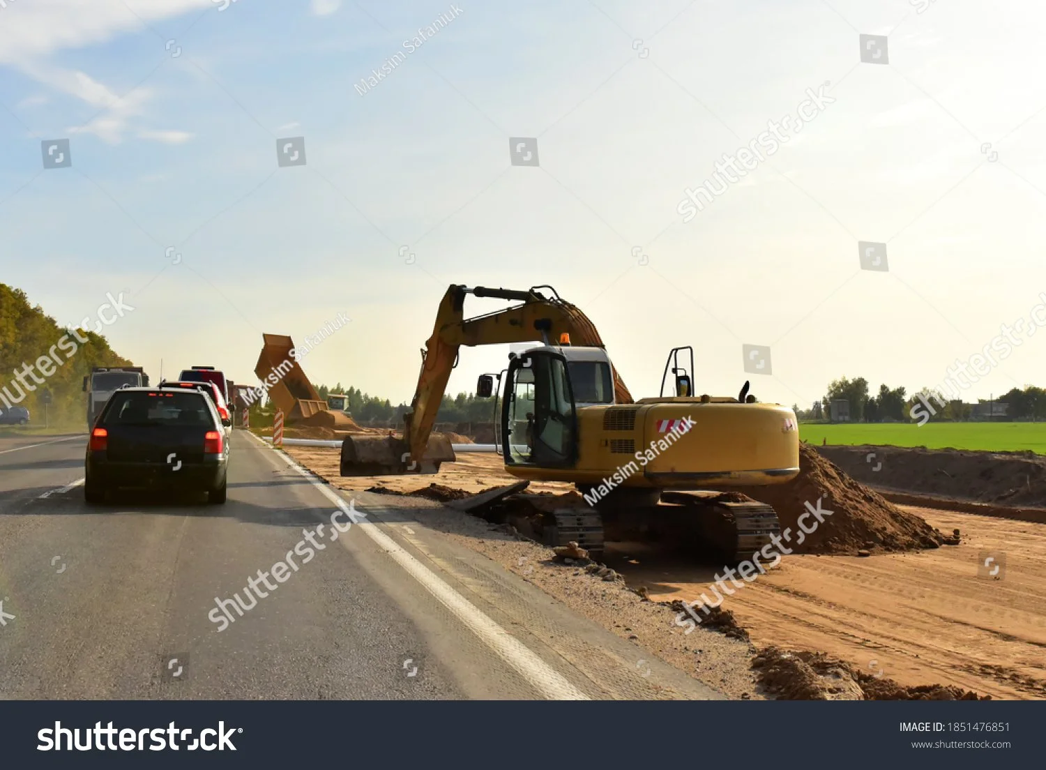 Road construction site with excavator and vehicles, clear sky.