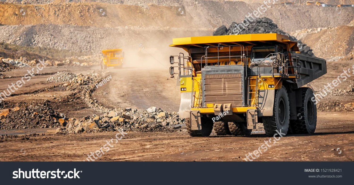 Yellow mining truck carrying rocks at a quarry with dusty terrain and another truck in the background.