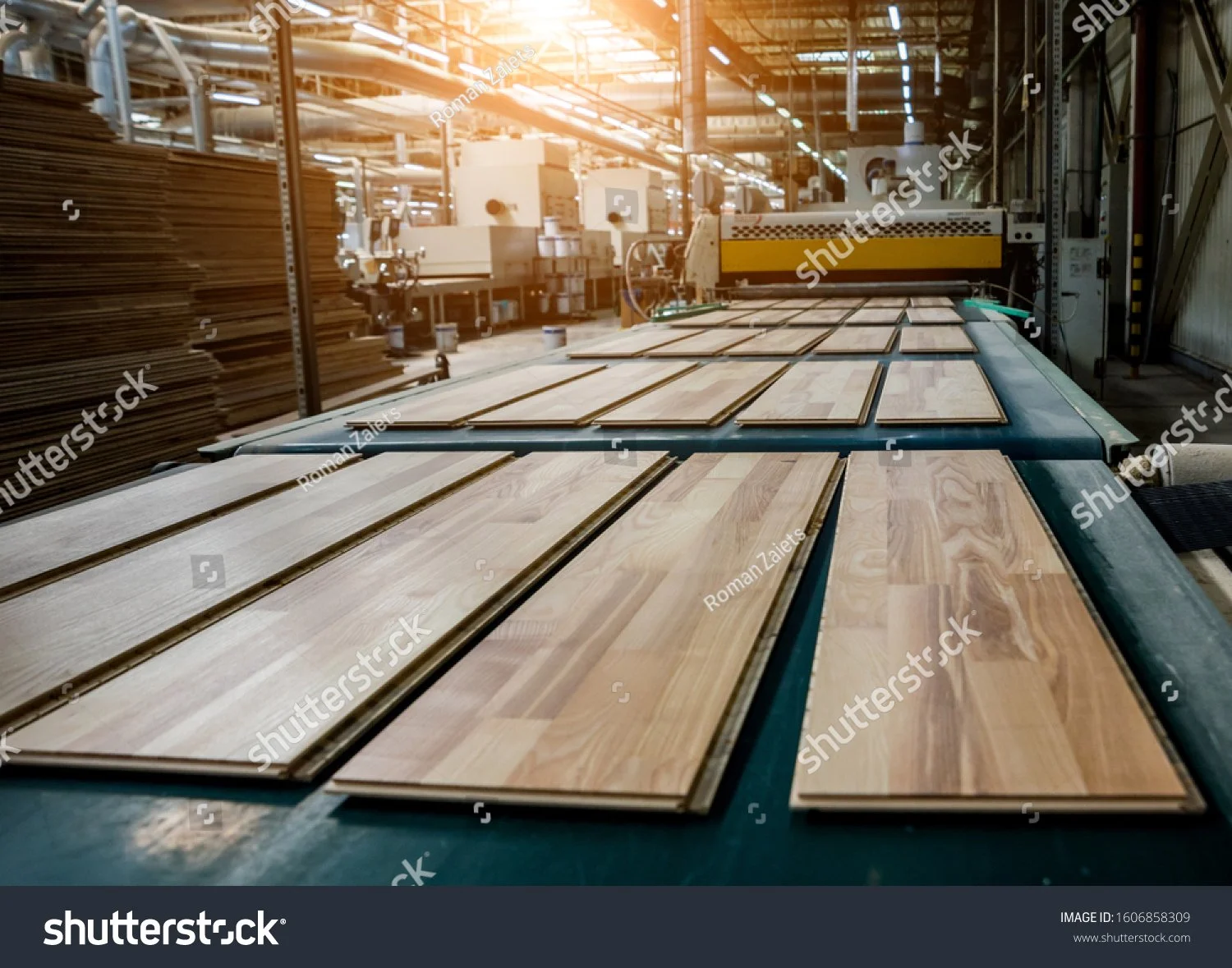 Laminate flooring planks on a production line in a factory with machinery in the background.