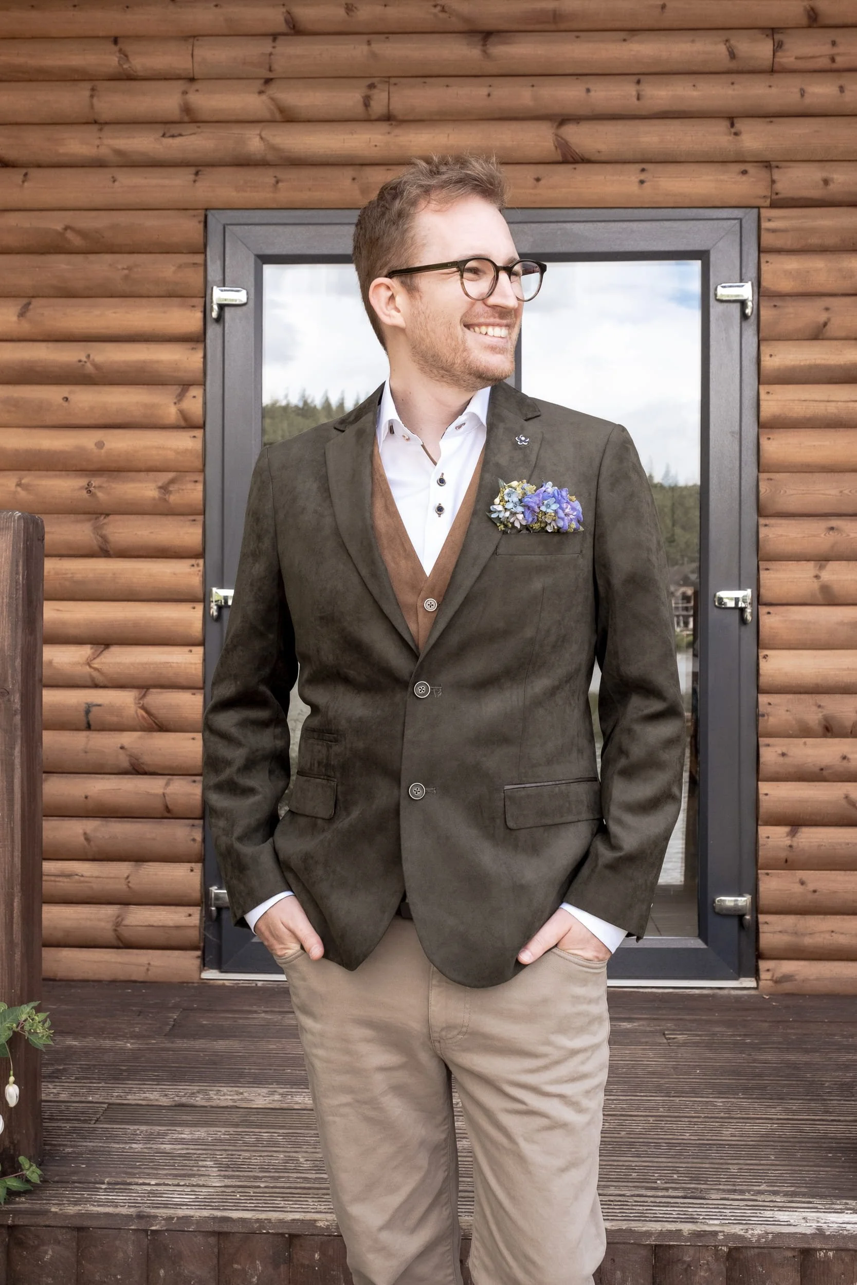 The groom at same sex wedding is smiling wearing his jacket with blue pocket floral square