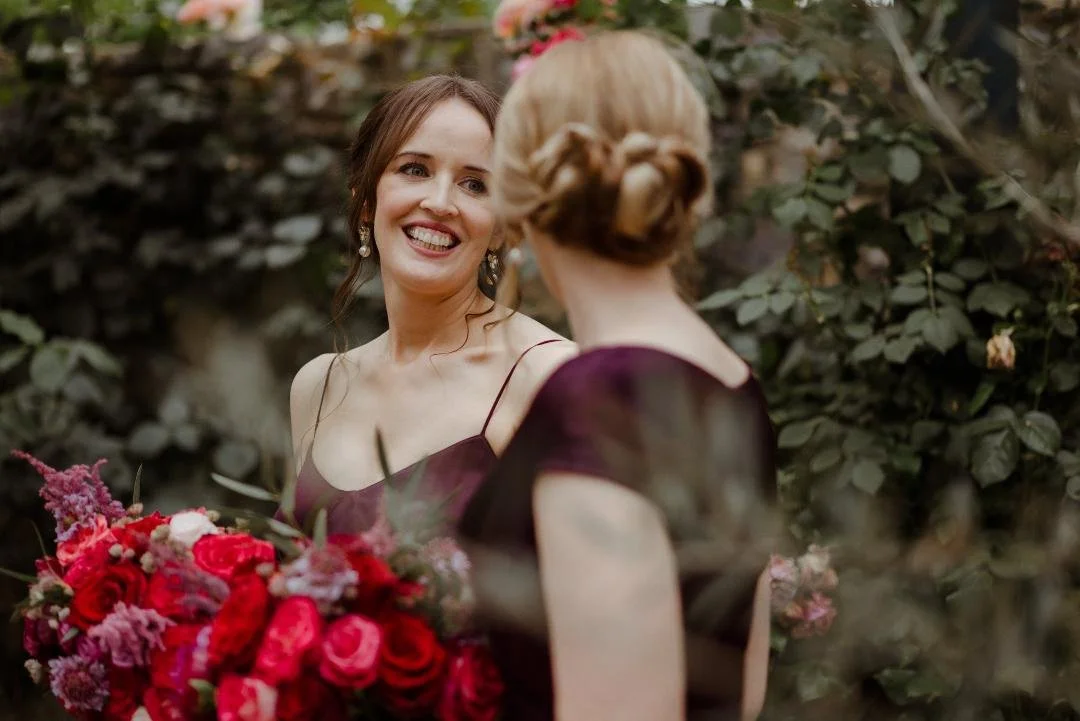 Bridesmaids chatting holding bouquets in luxurious colours with burgundy peonies. bright pink and deep red roses, soft pink scabious and astilbe