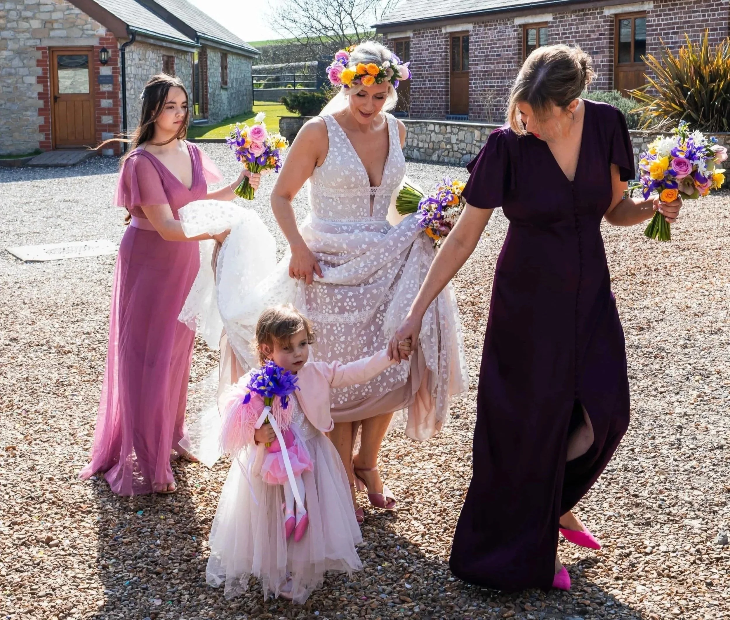 The bridal party are walking to Rosedew ceremony room holding their seasonal spring wedding flower bouquets. The bride is wearing a full spring flower floral crown