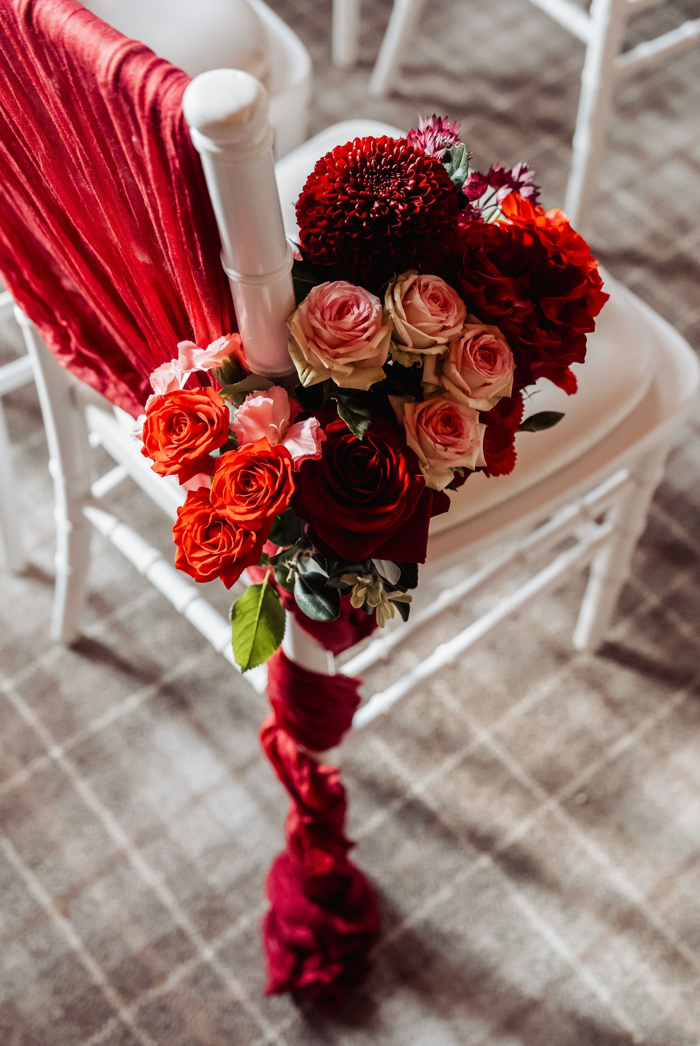 Floral bouquets of deep reds and rose colours attached to the aisle chairsat Hensol Castle