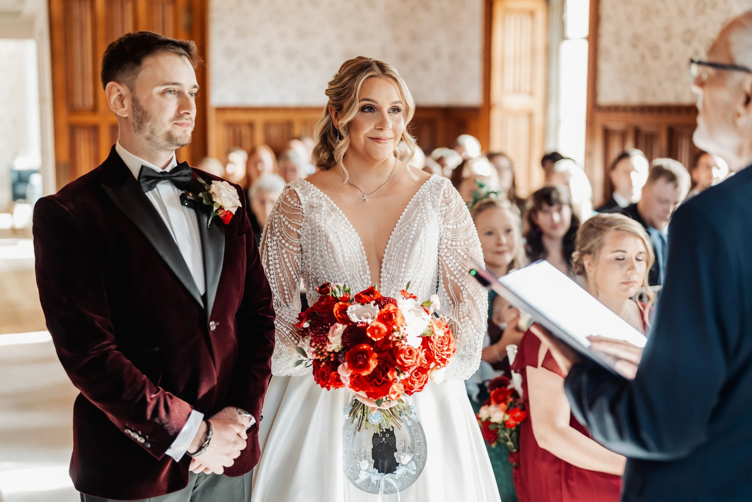 The bride and groom getting married at Hensol Castle. The bride is holding her bouquet full of deep red, crimson and pink flowers