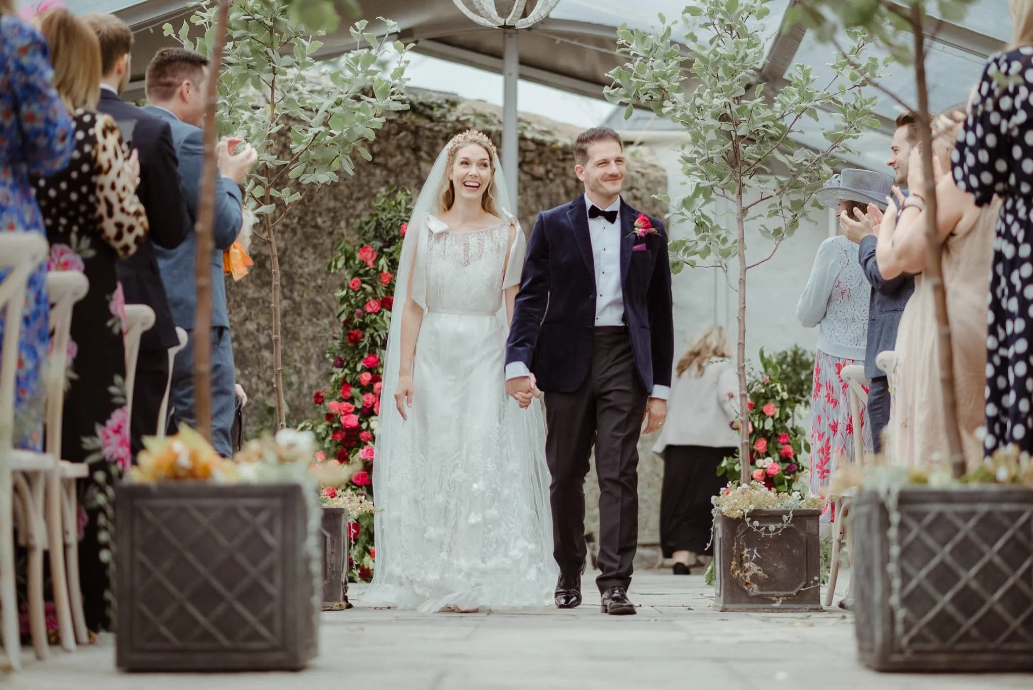 Walking down the aisle as Mr and Mrs floral pillars stand behind, olive trees line the aisle