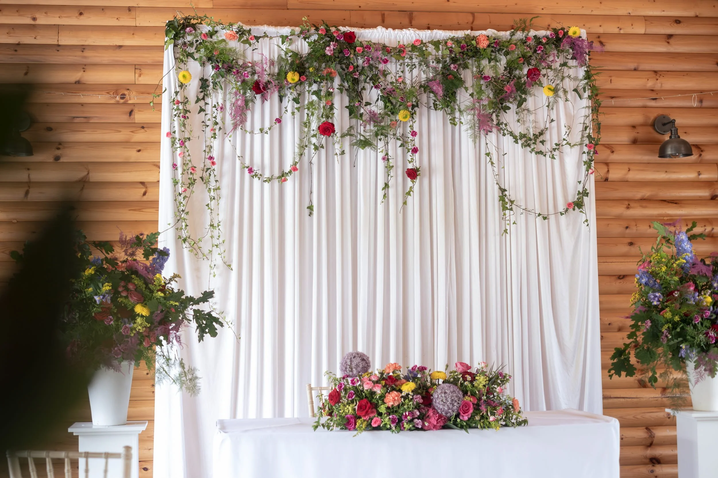 Colourful wedding flowers at Rhodris by the Lake with floral backdrop, floral urns and long and low table arrangement