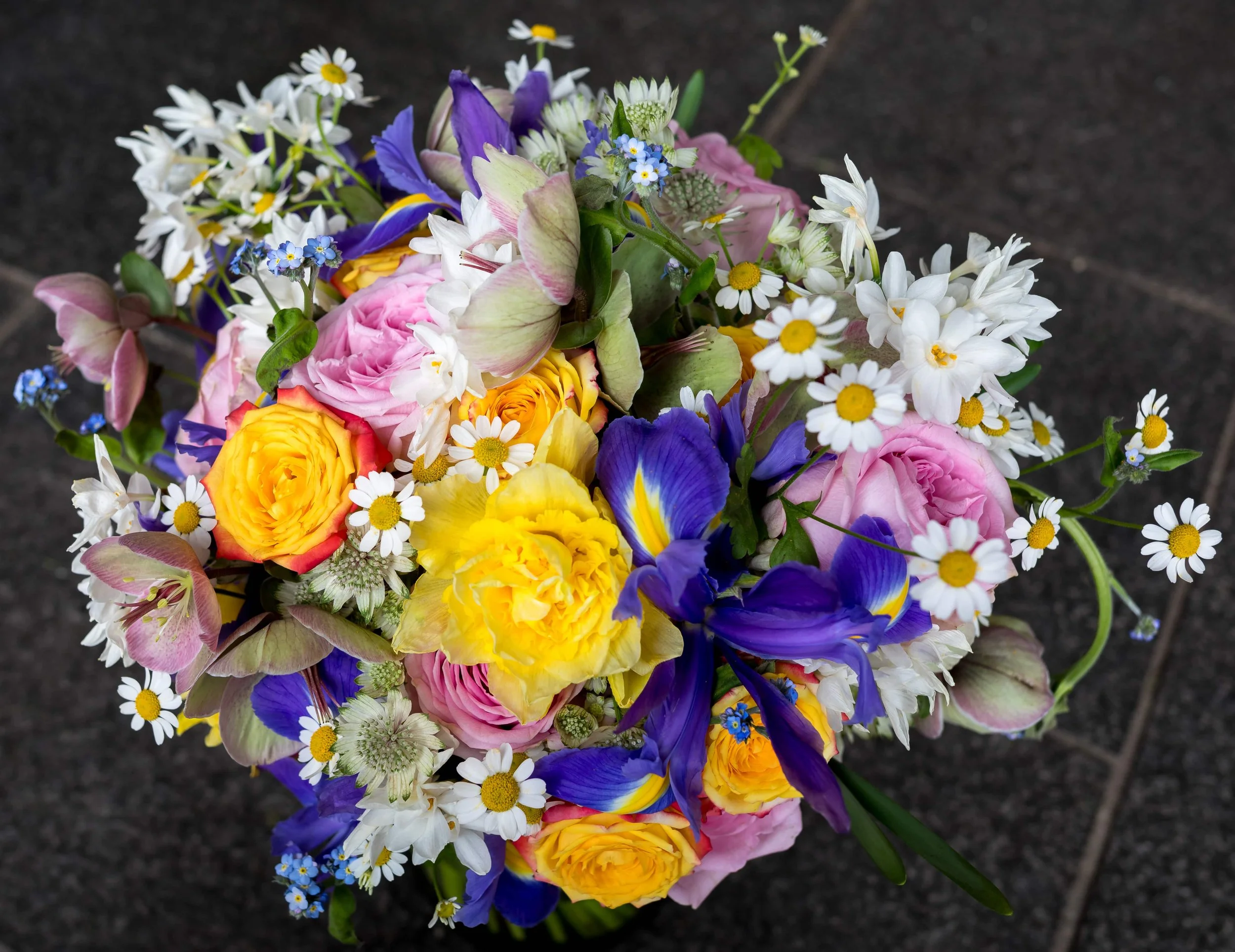 A view from above the wedding flower bridal bouquet full of colourful spring flowers of iris, narcissus, astrantia, daisies, helebores, daffodils and roses
