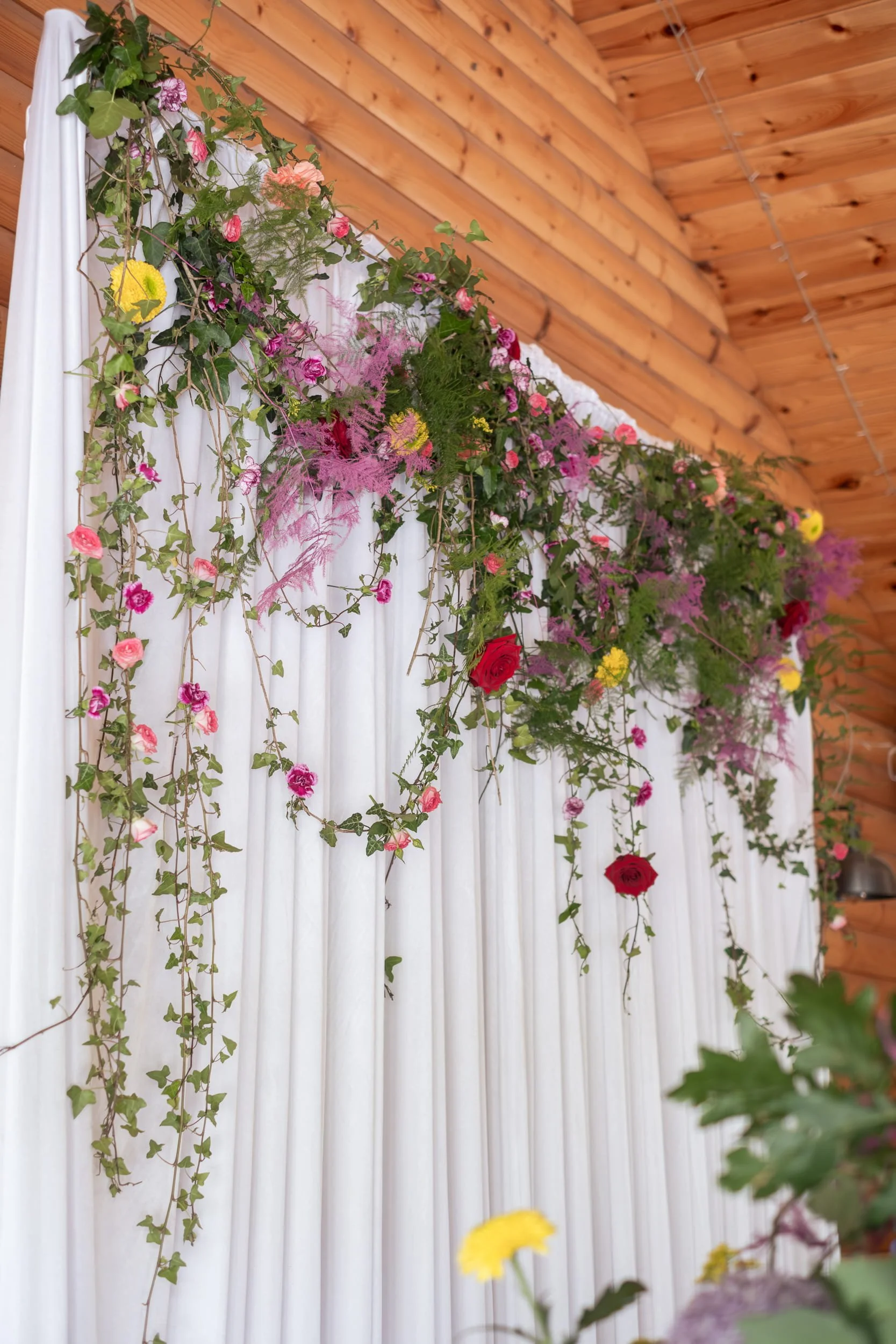Cascading colourful flowers over draping materials for the ceremony focal point