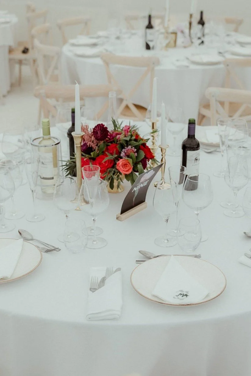 Table centrepiece with wedding flowers in burgundy, deep red and pinks surrounded by brass candlesticks