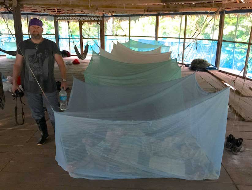 Peruvian Amazon Loreto, Peru – Along the banks of a small tributary. Jake stands in front of our second layer of defense against the busy Amazonian mosquitoes in Mosquito Net Row in the “Kiva” building. The first layer is the mosquito screen enrobing the entire “Kiva” hut, the second of course our “night chambers” where we took refuge from the ones who got into the Kiva. Sleeping on a wood floor with little padding was easy after tracking through mud and jungle all day, we would return, eat and sleep.
