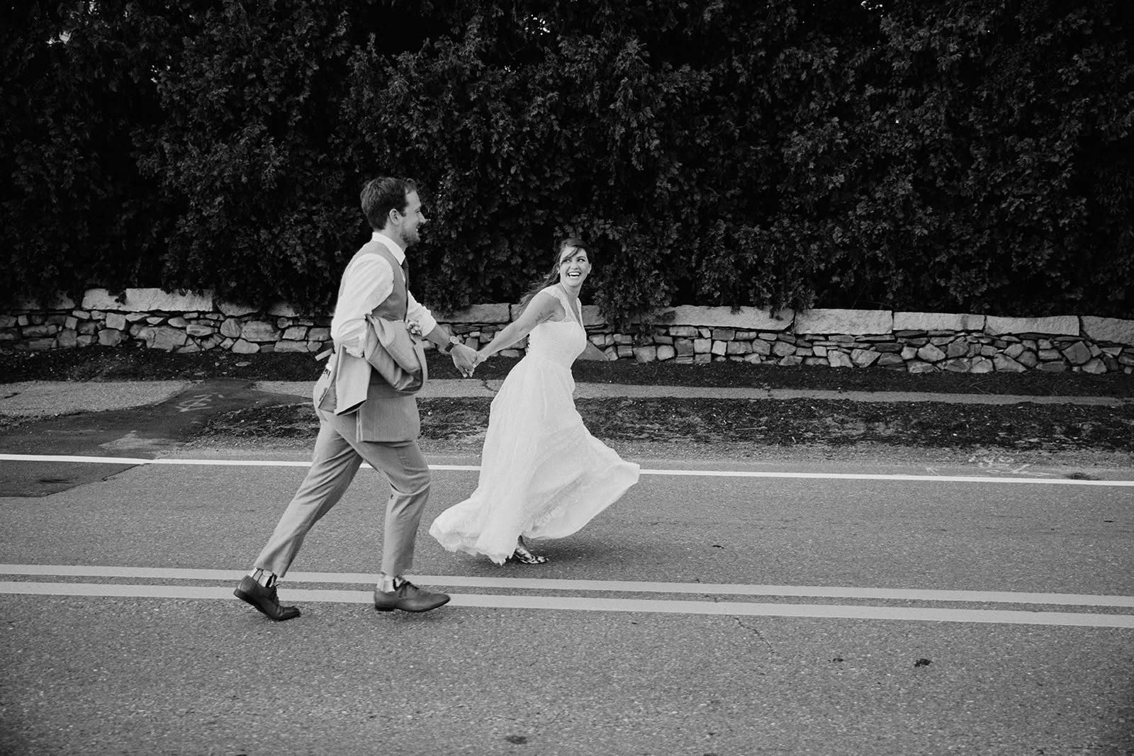 The bride and groom hold hands while running across the street