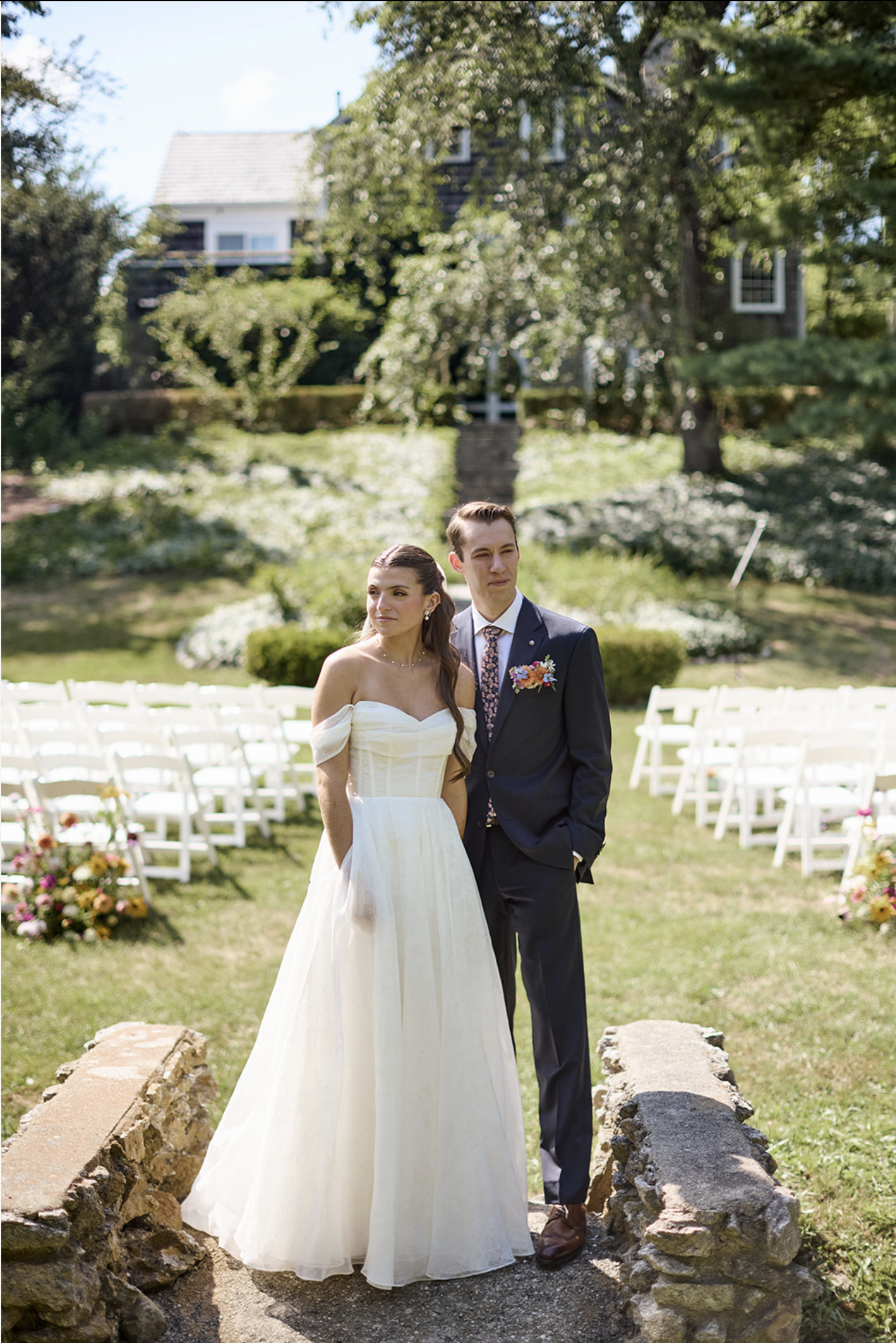 A wedding couple stands on a stone bridge in a green field at Overbook House at Bay End Farm on Cape Cod