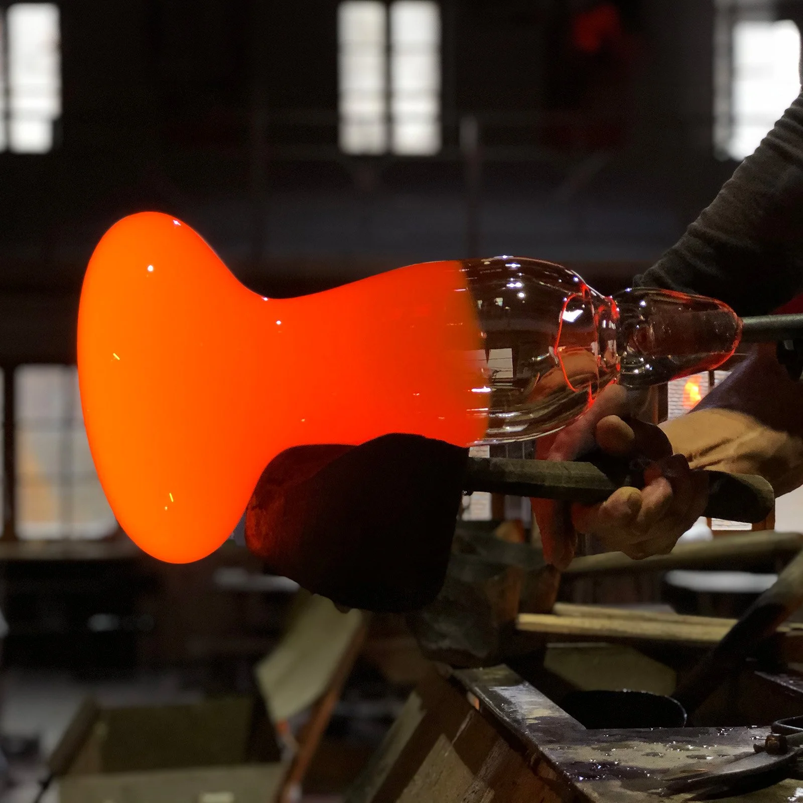 Craftsman shaping glowing glass with traditional wooden tool.