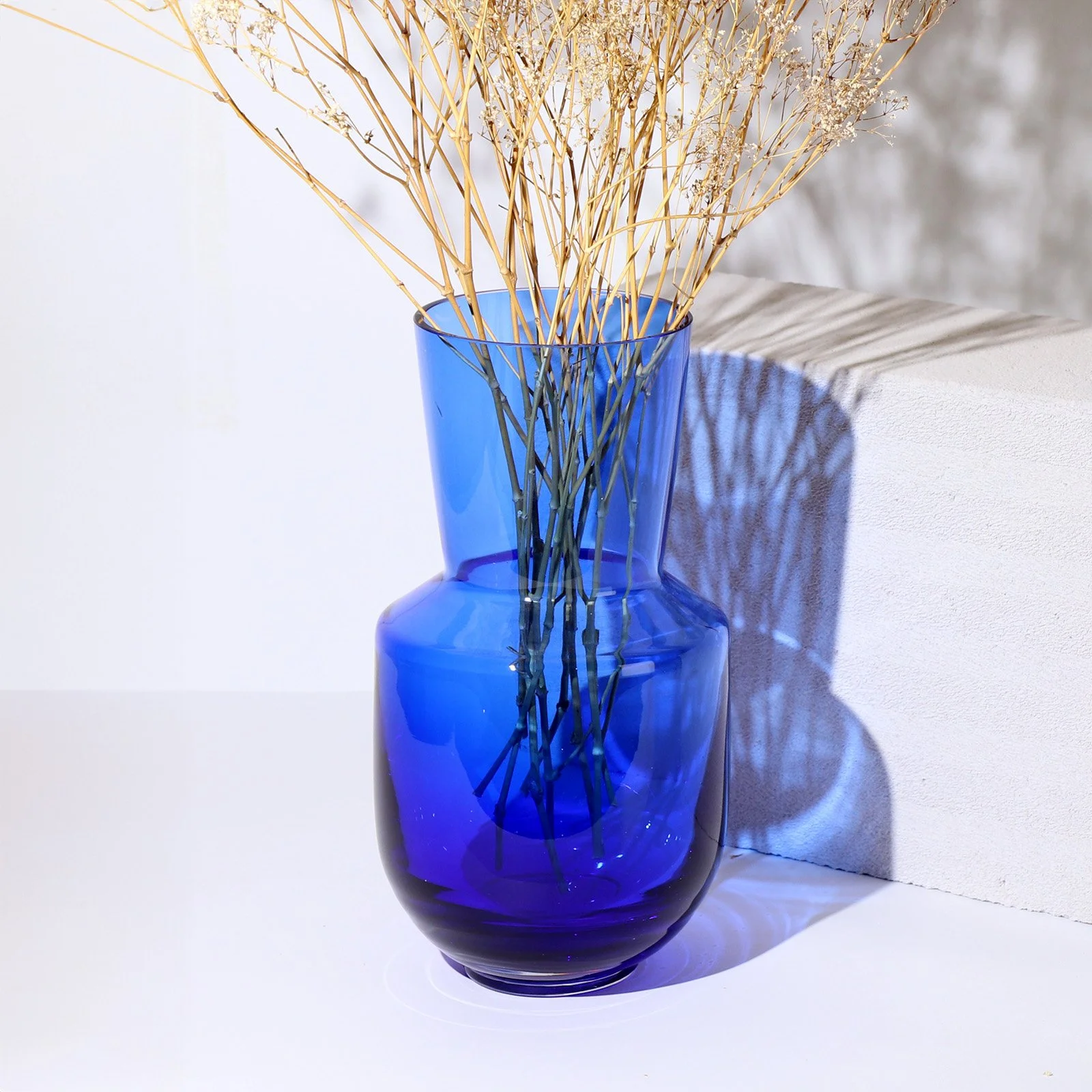 Blue glass vase with dried grass beside a white stone.
