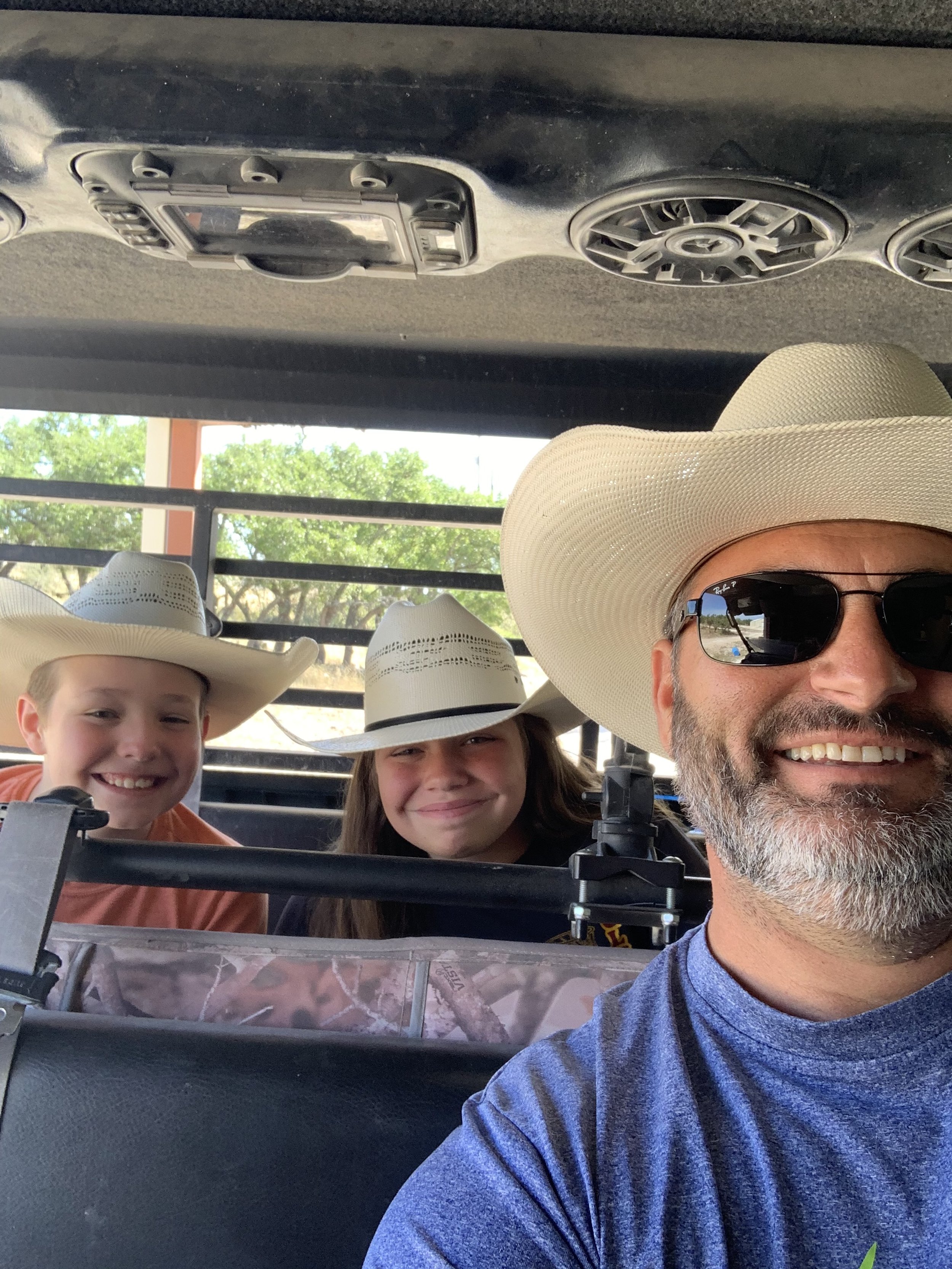 Two children and an adult wearing cowboy hats and sunglasses inside a vehicle.