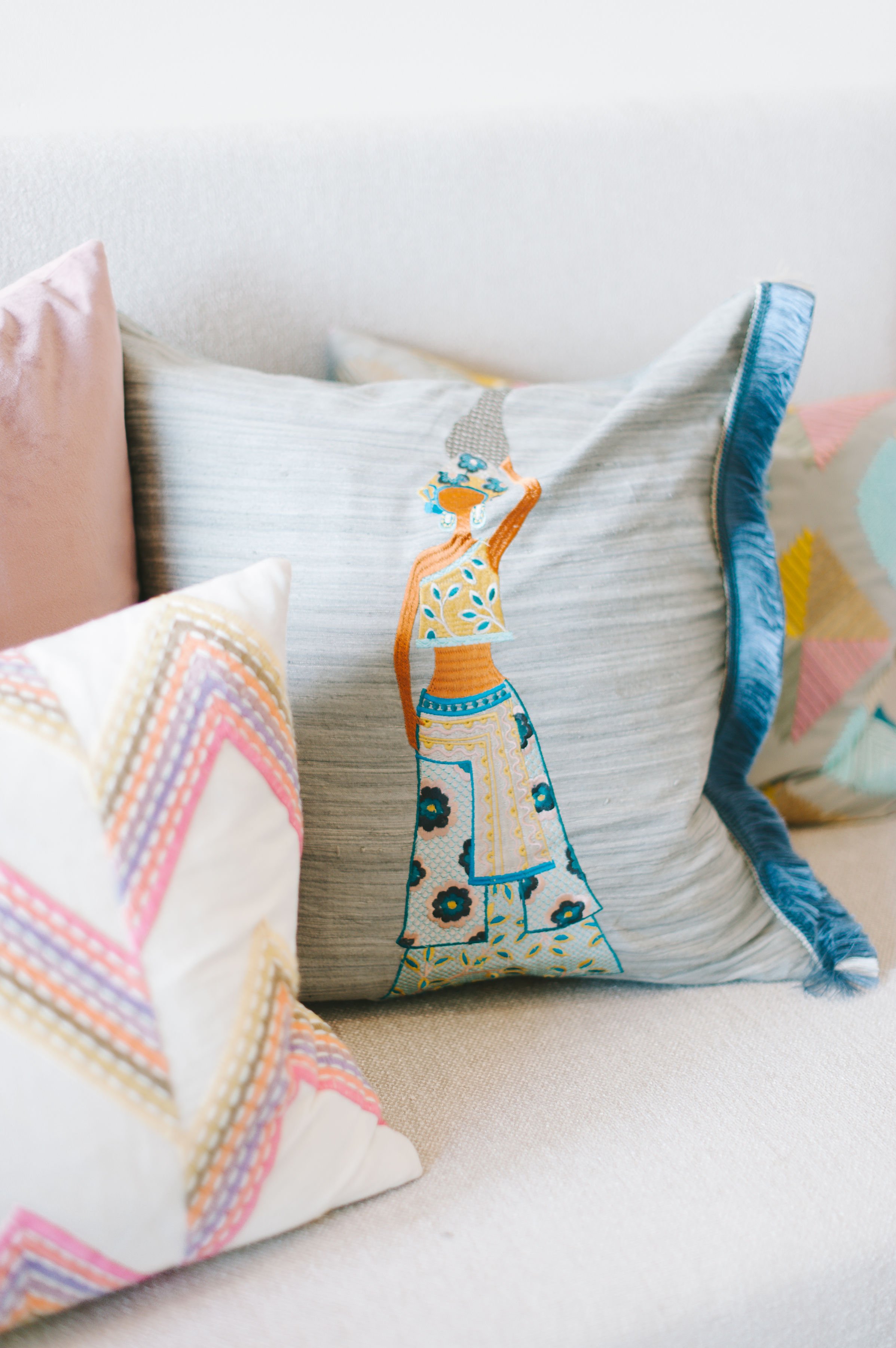 Verschiedene Kissen mit bunten, geprägten Stickereien auf einem Sofa.