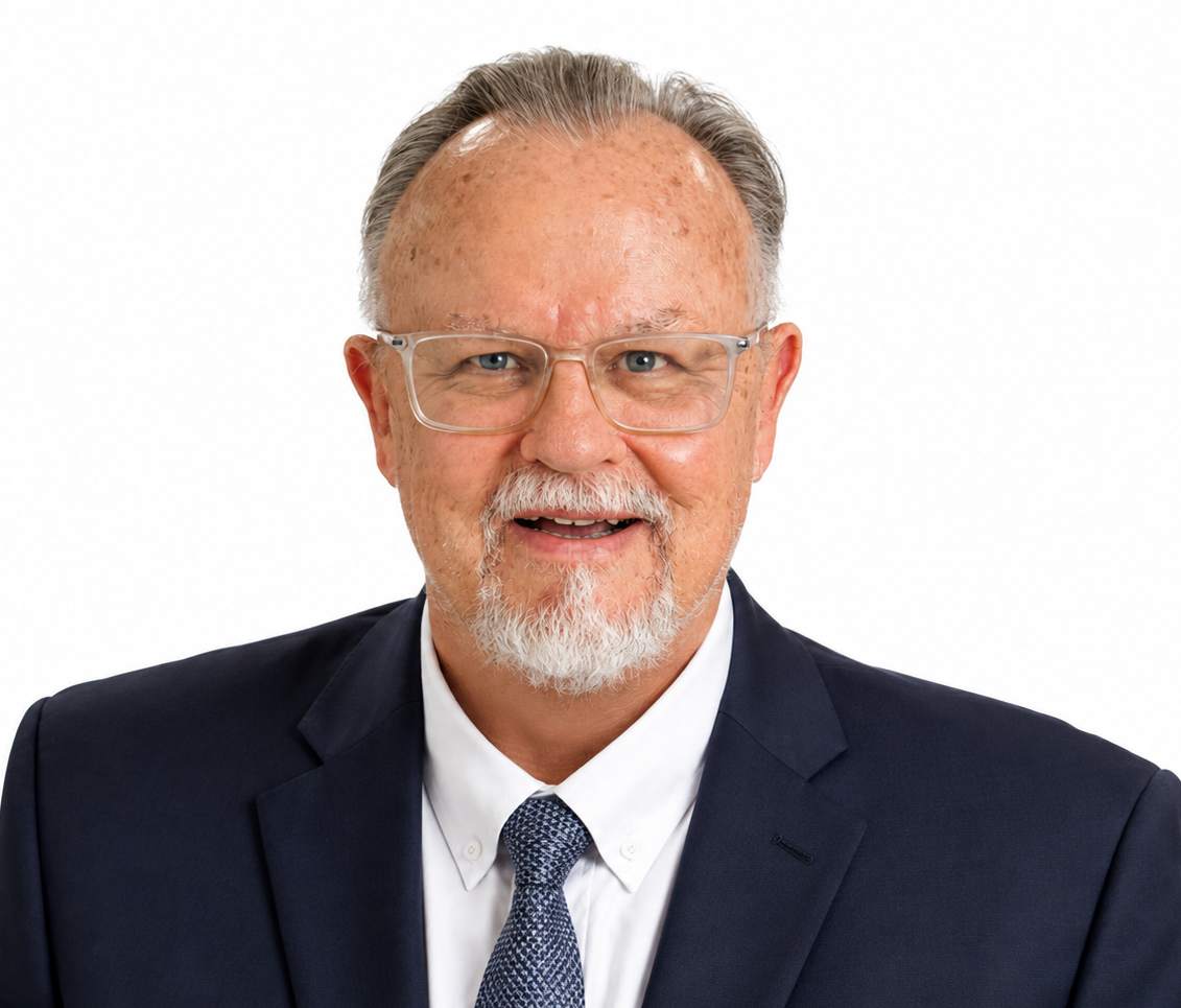 Portrait of an older man with glasses, light-colored suit, and patterned tie smiling against a white background.