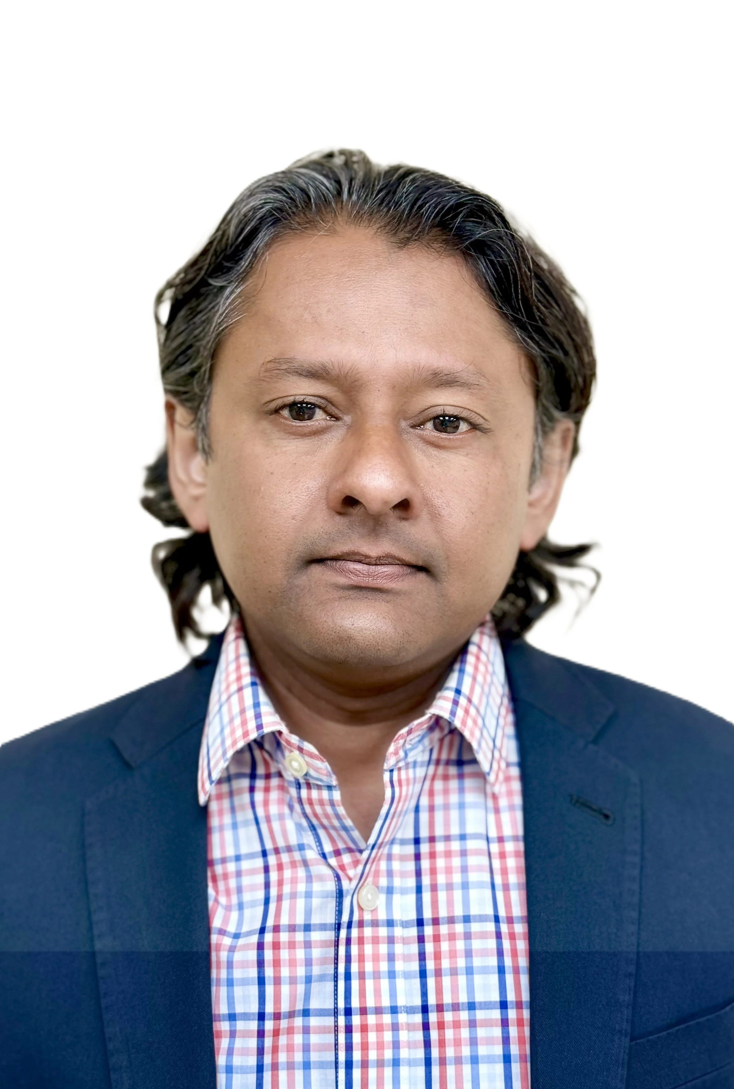 Headshot of a man with medium-length dark hair, wearing a dark blazer over a red, white, and blue checked shirt, against a white background.