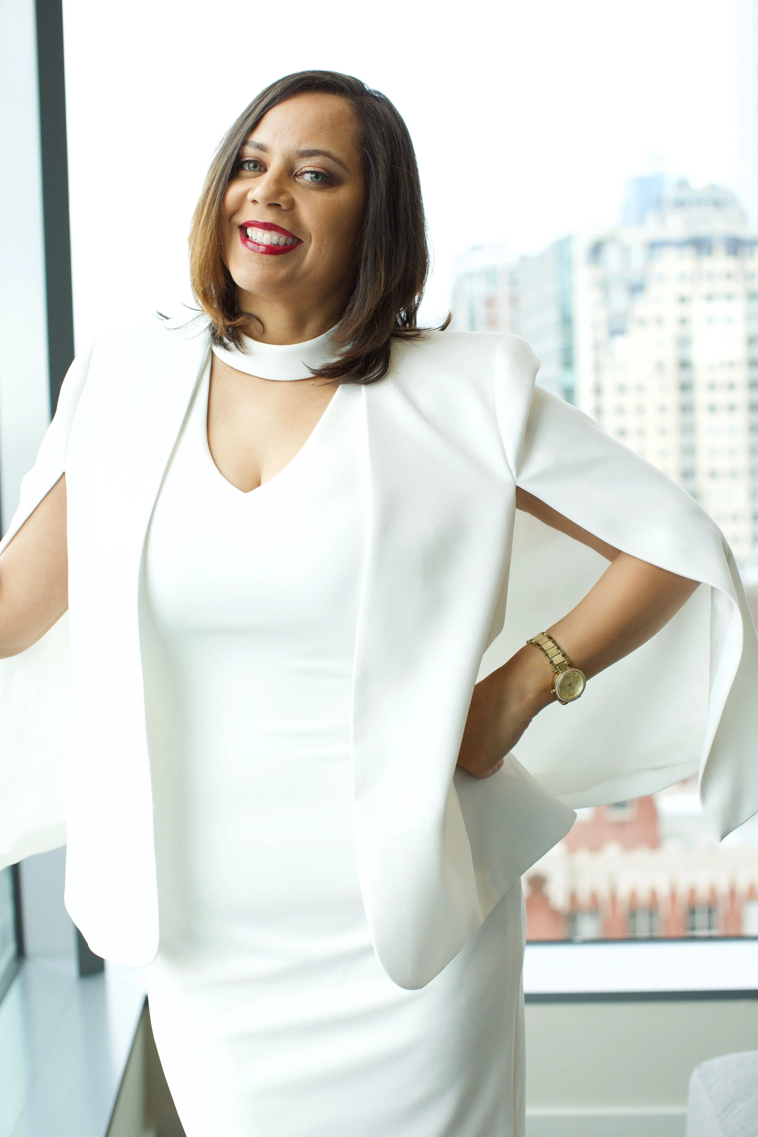 Denise Ransom Harris smiling in a white cape dress beside a city window