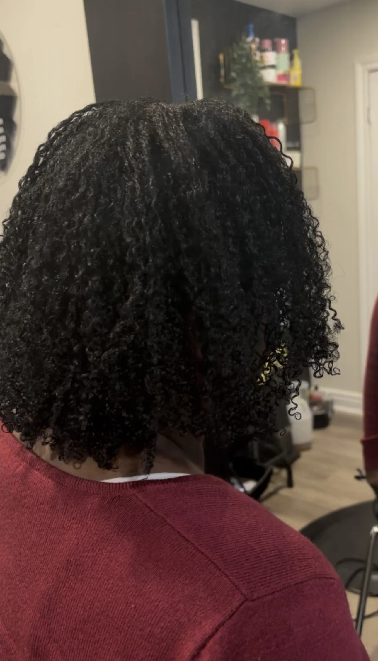 Close-up of a woman with braided hairstyle, wearing small earrings, with her eyes closed, against a green leafy background.