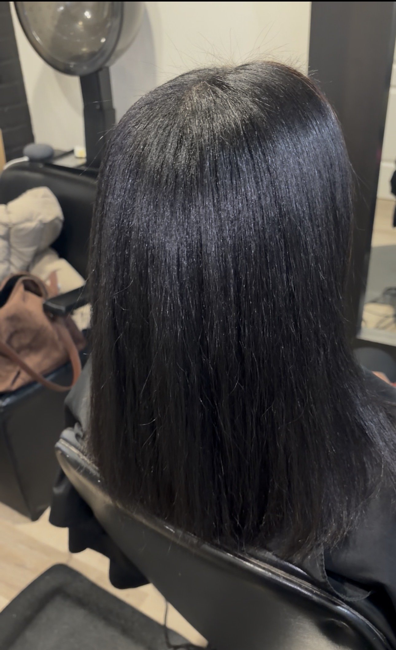 Top view of wavy, blonde hair with darker roots against a green leafy background.