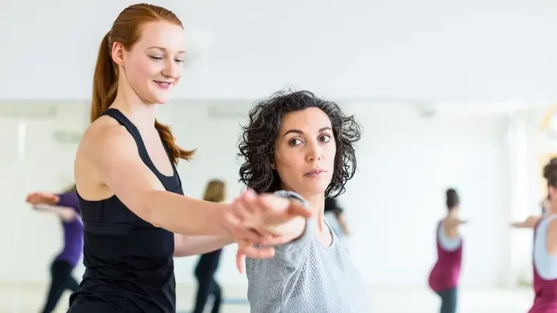 Instructor assisting student in Warrior 2 pose.