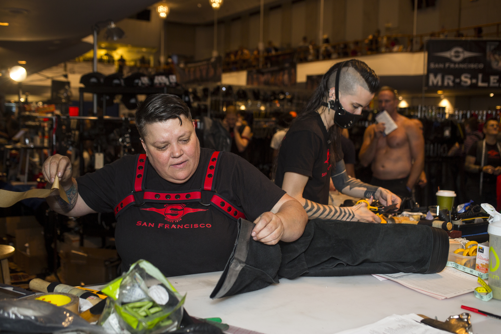  Skuwish, center, and Jackzon, right, work at the Mr S Leather booth in the gear market, hemming and adjusting just purchased leather wear. The Mr S Leather company also donates the winners' sash for The 40th Annual International Mister Leather Compe