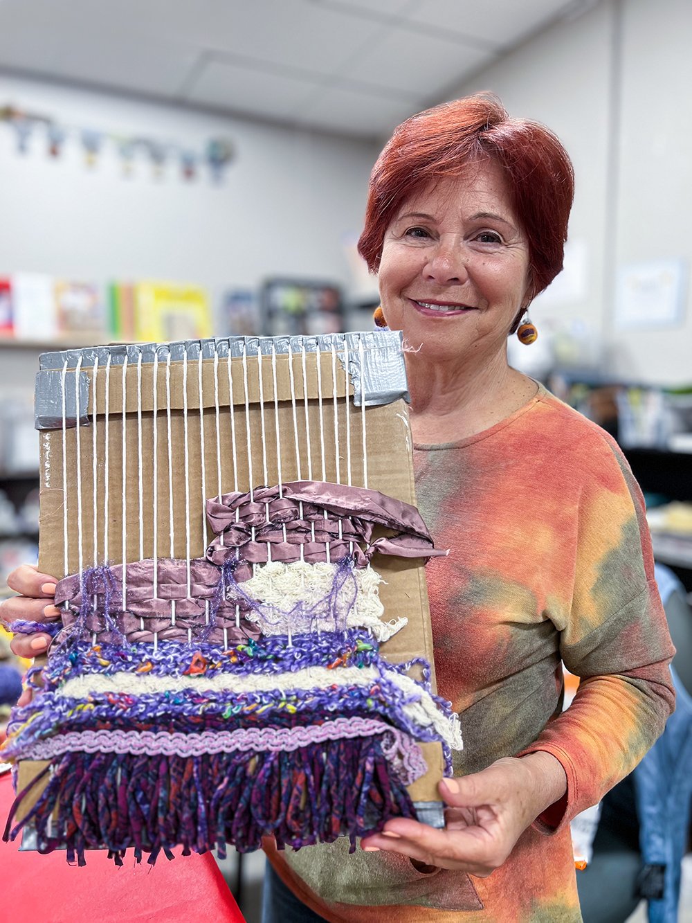 Woman holding up cardboard loom with weaving