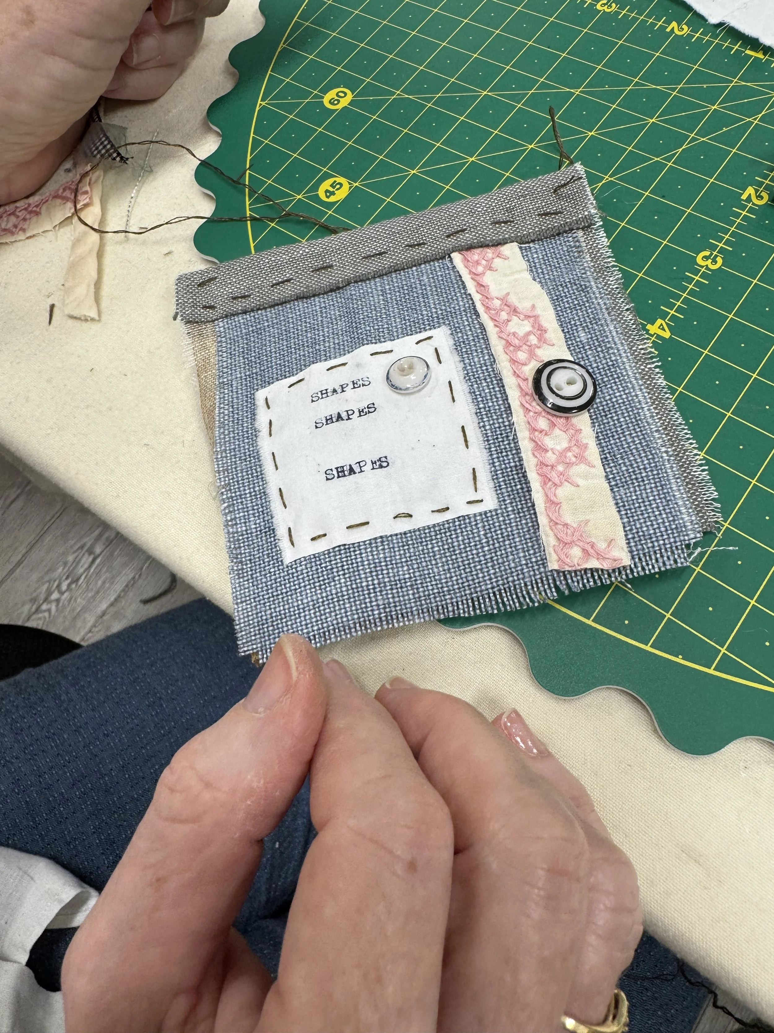 Small fabric book made with blue fabric, buttons and white square with typed text ("SHAPES")
