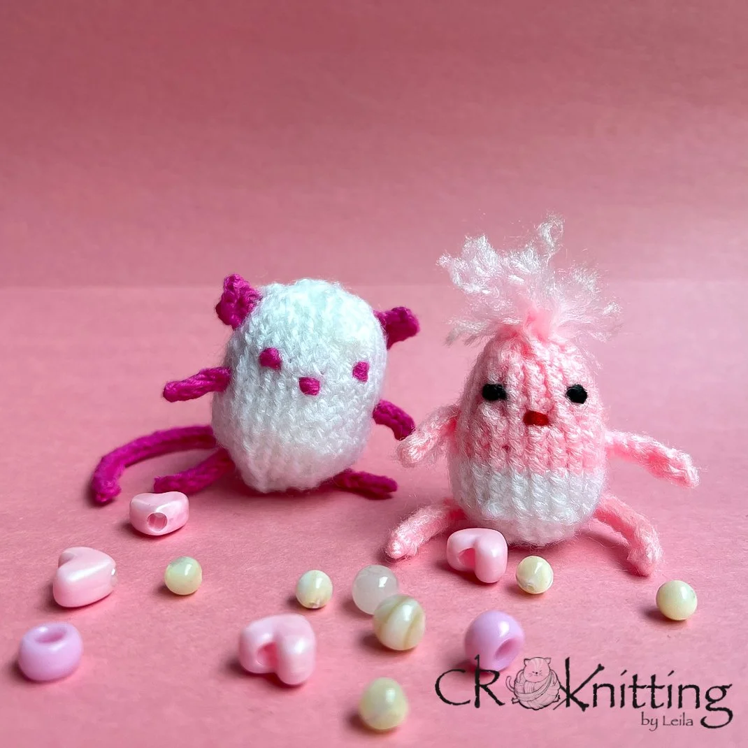Two small knit animals made out of pink and white yarn