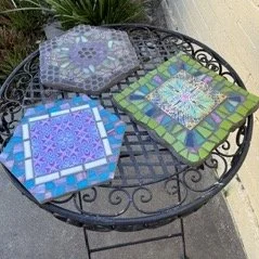 Three colorful tile trivets on a garden table