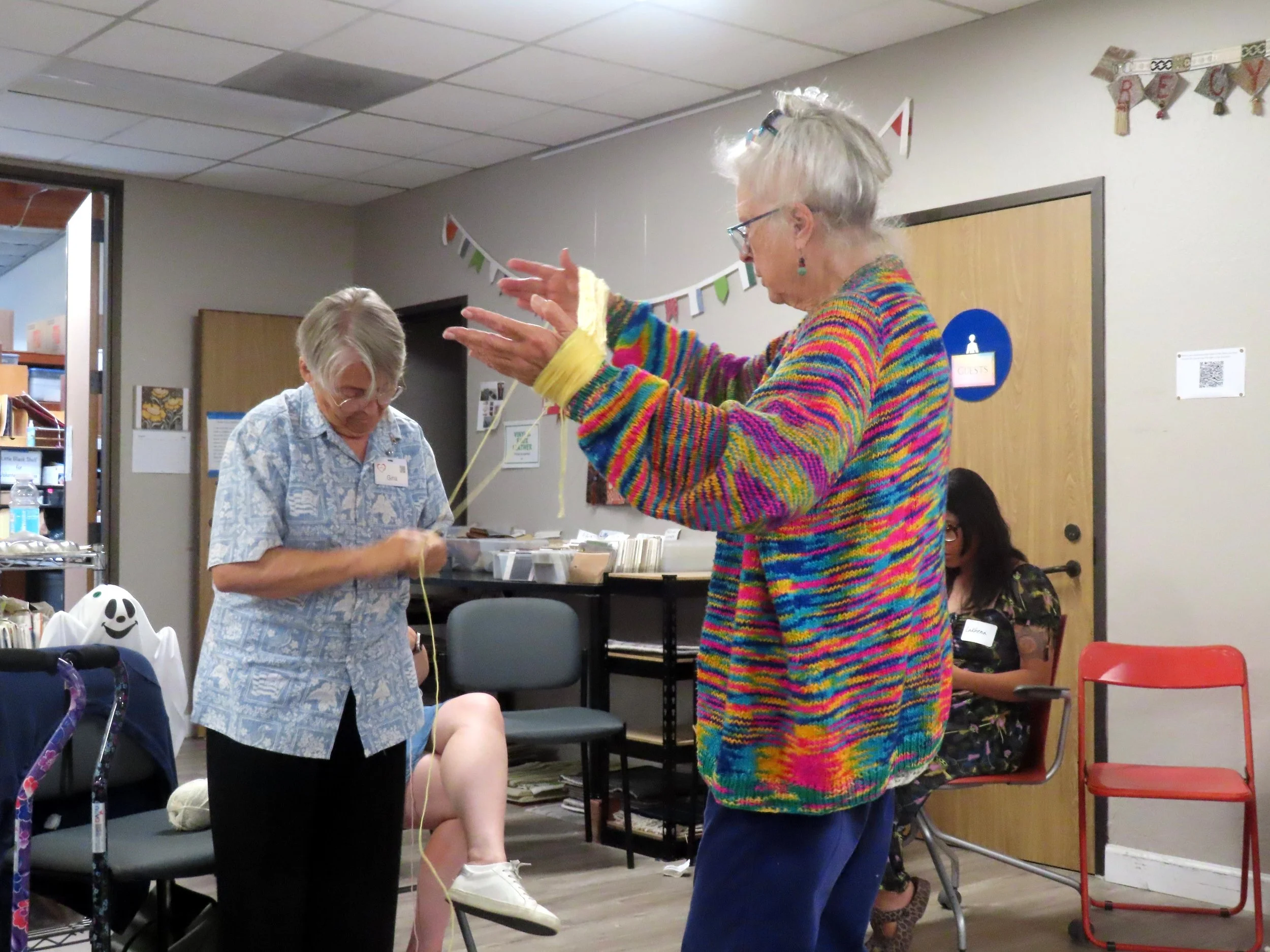 Two standing women holding long piece of yarn in their hands
