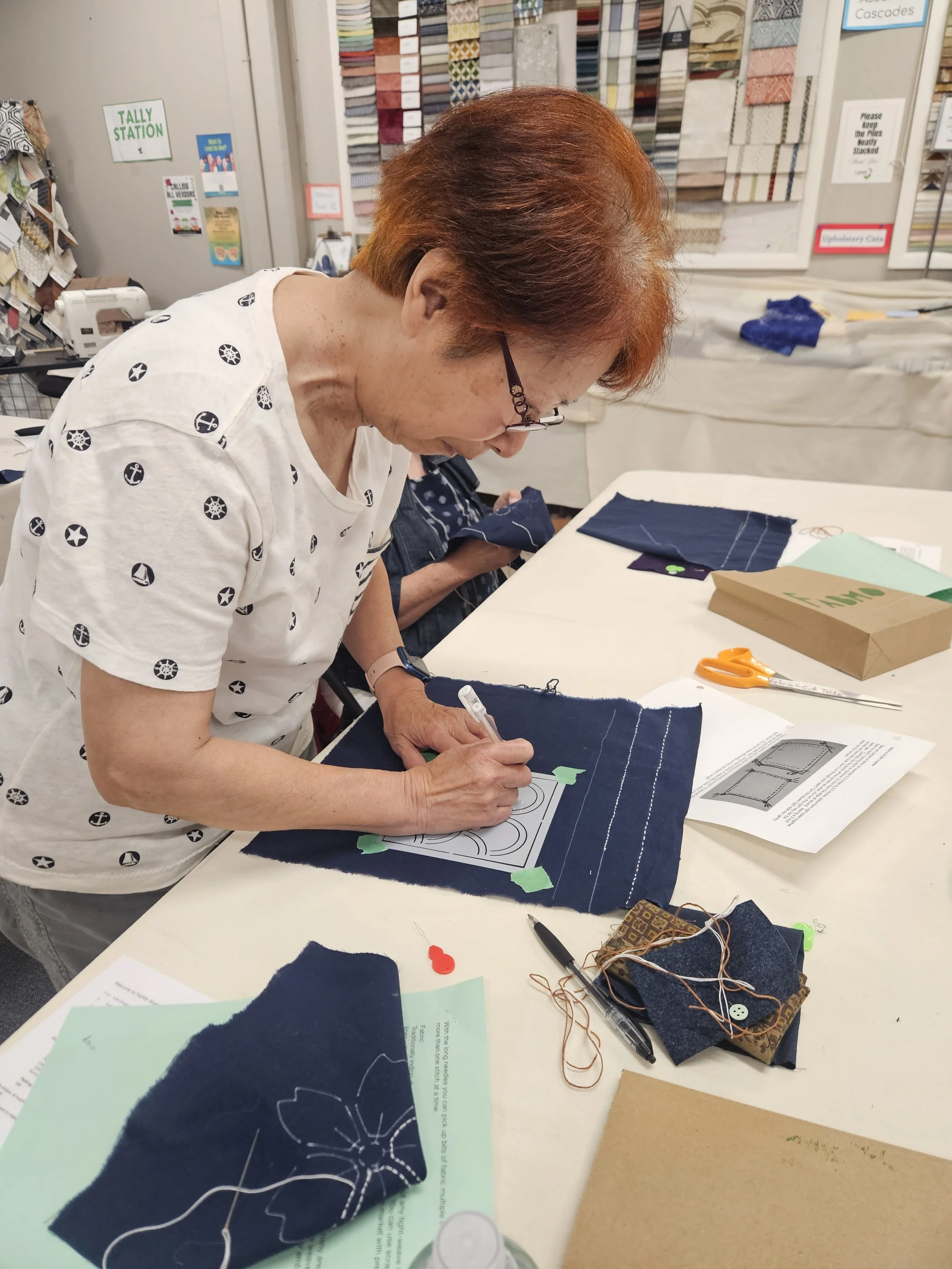 Red-haired woman standing at table marking lines on dark fabric