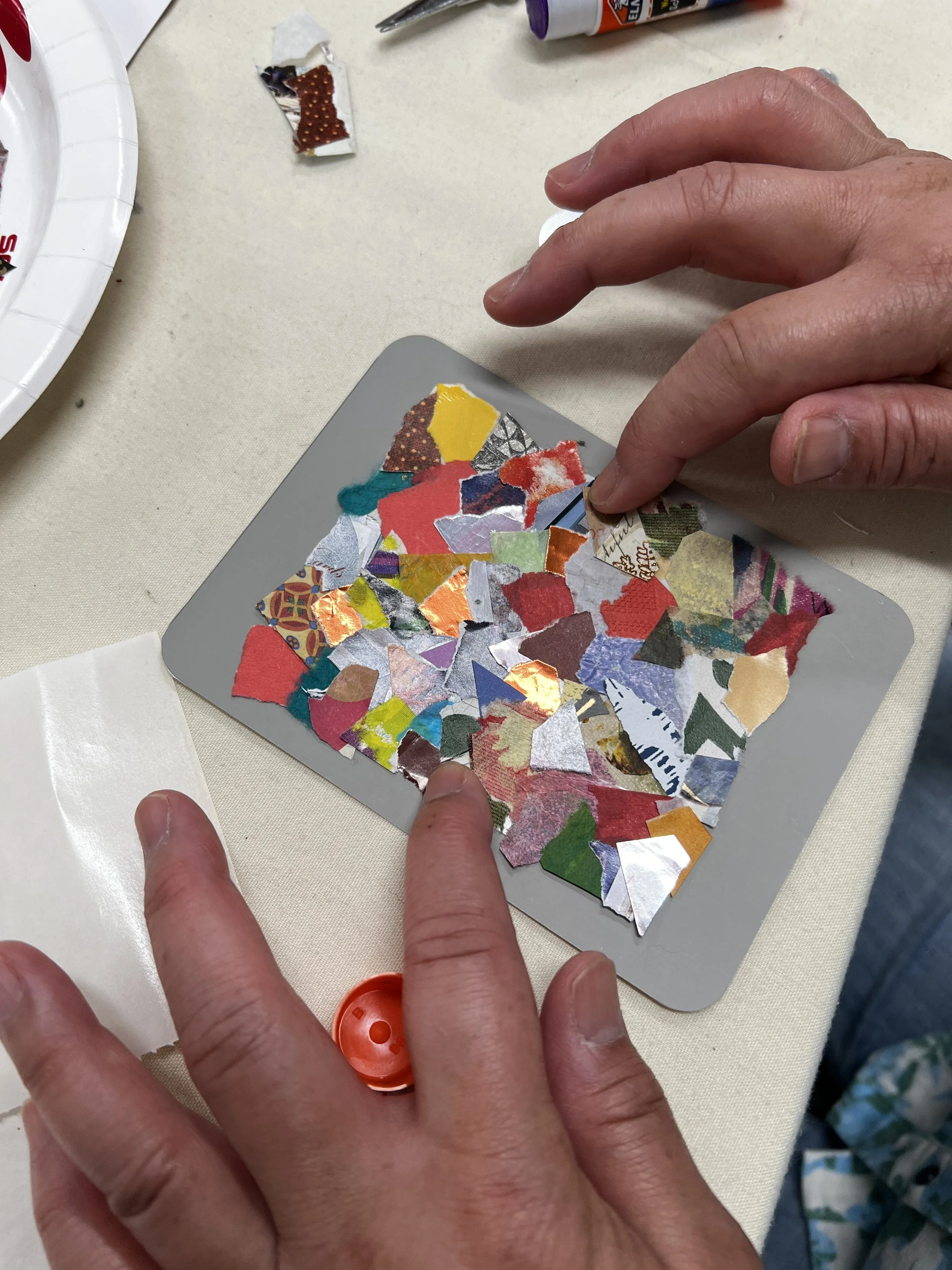 Colorful paper collage greeting card on grey background framed by two hands