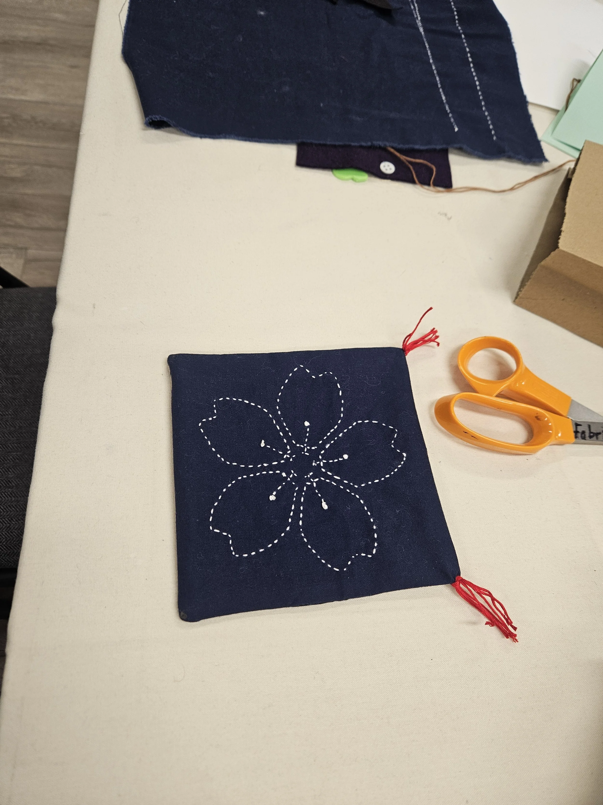 Flower design in white stitches on dark blue fabric square