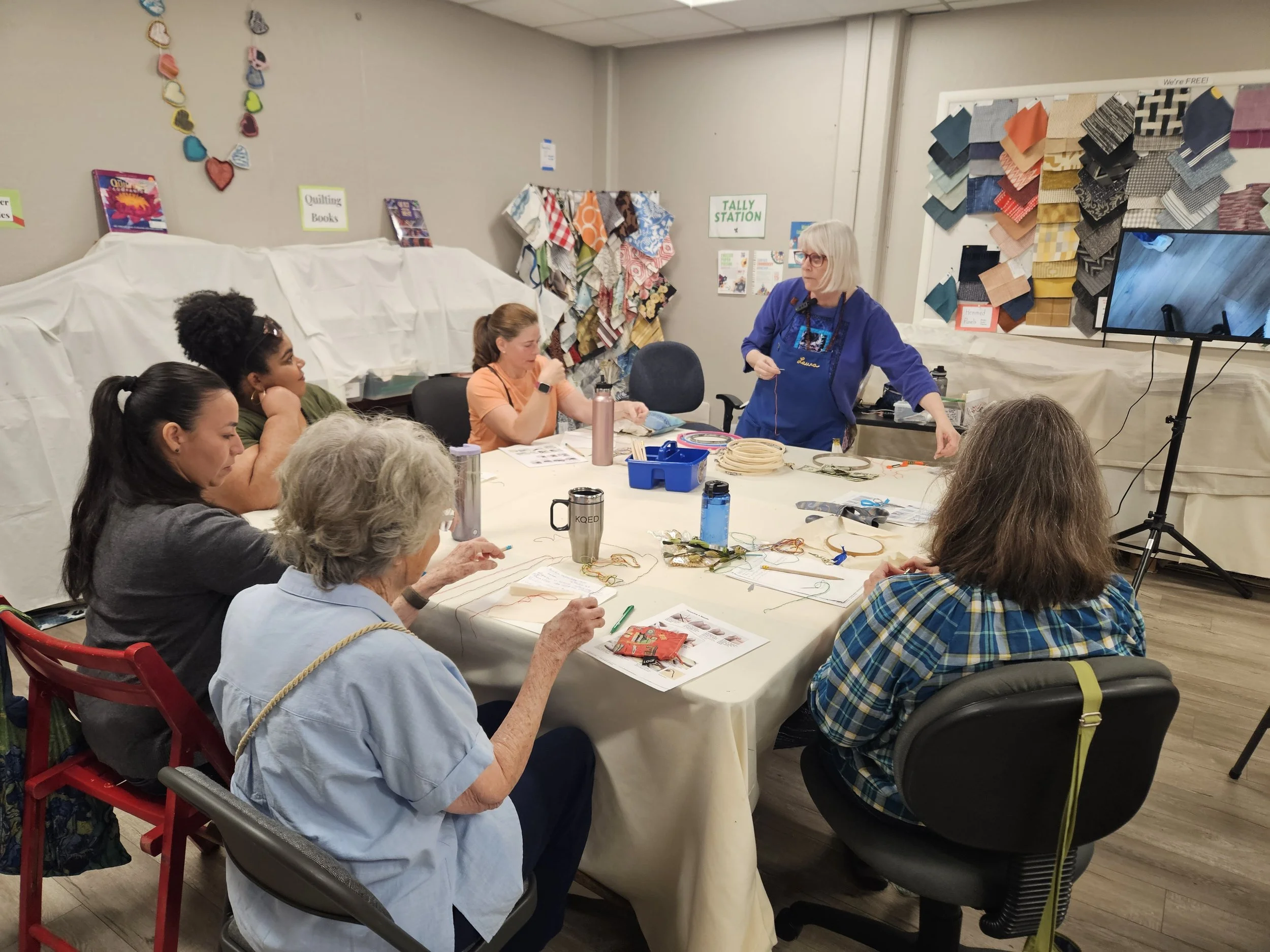 Group of people seated around table learning how to embroider