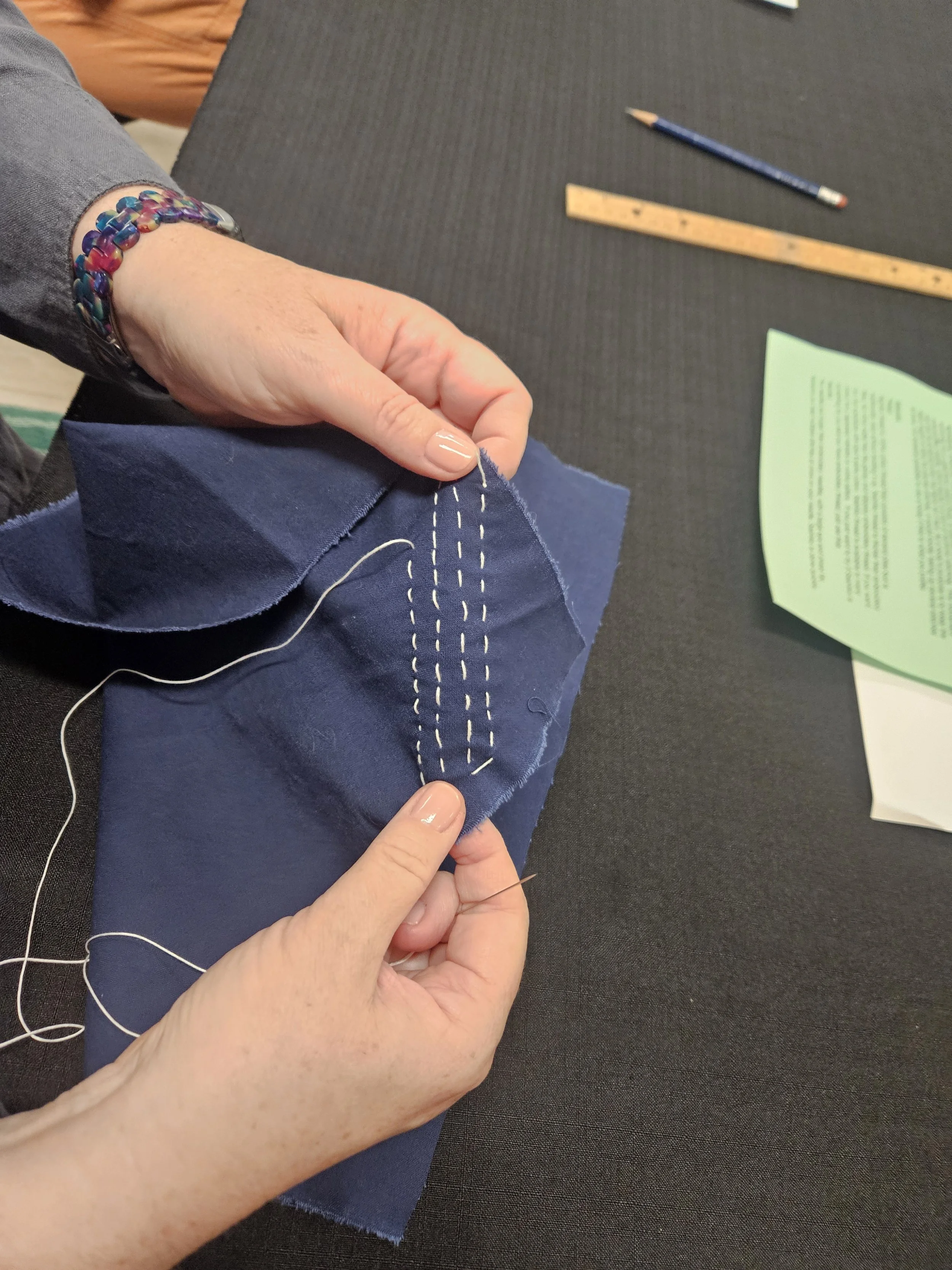 Hands holding navy blue fabric with white stitches