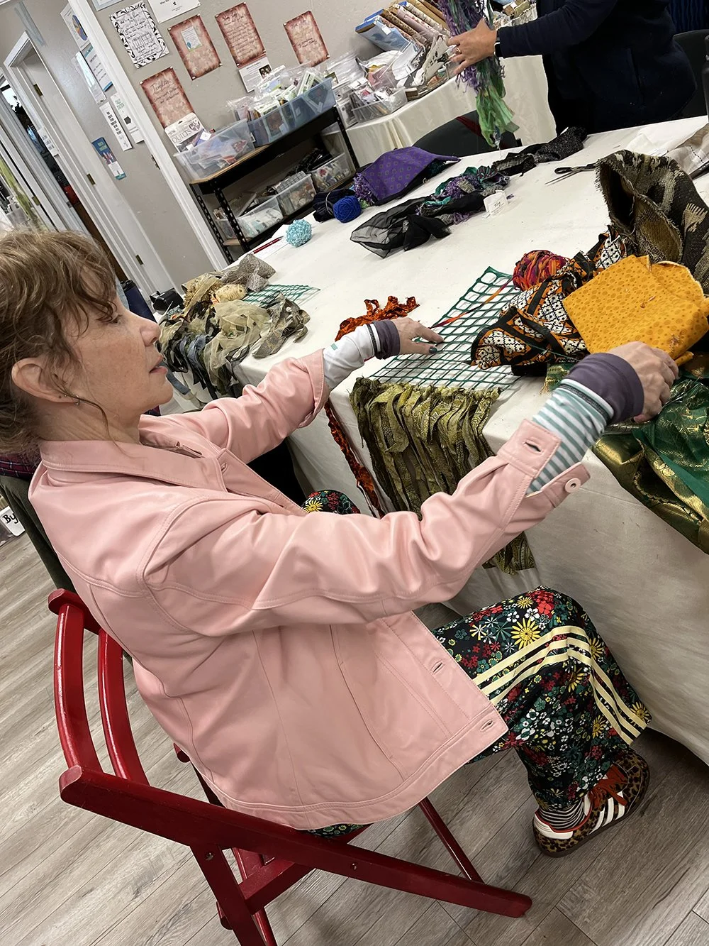 Seated woman in pink jacket working on weaving project