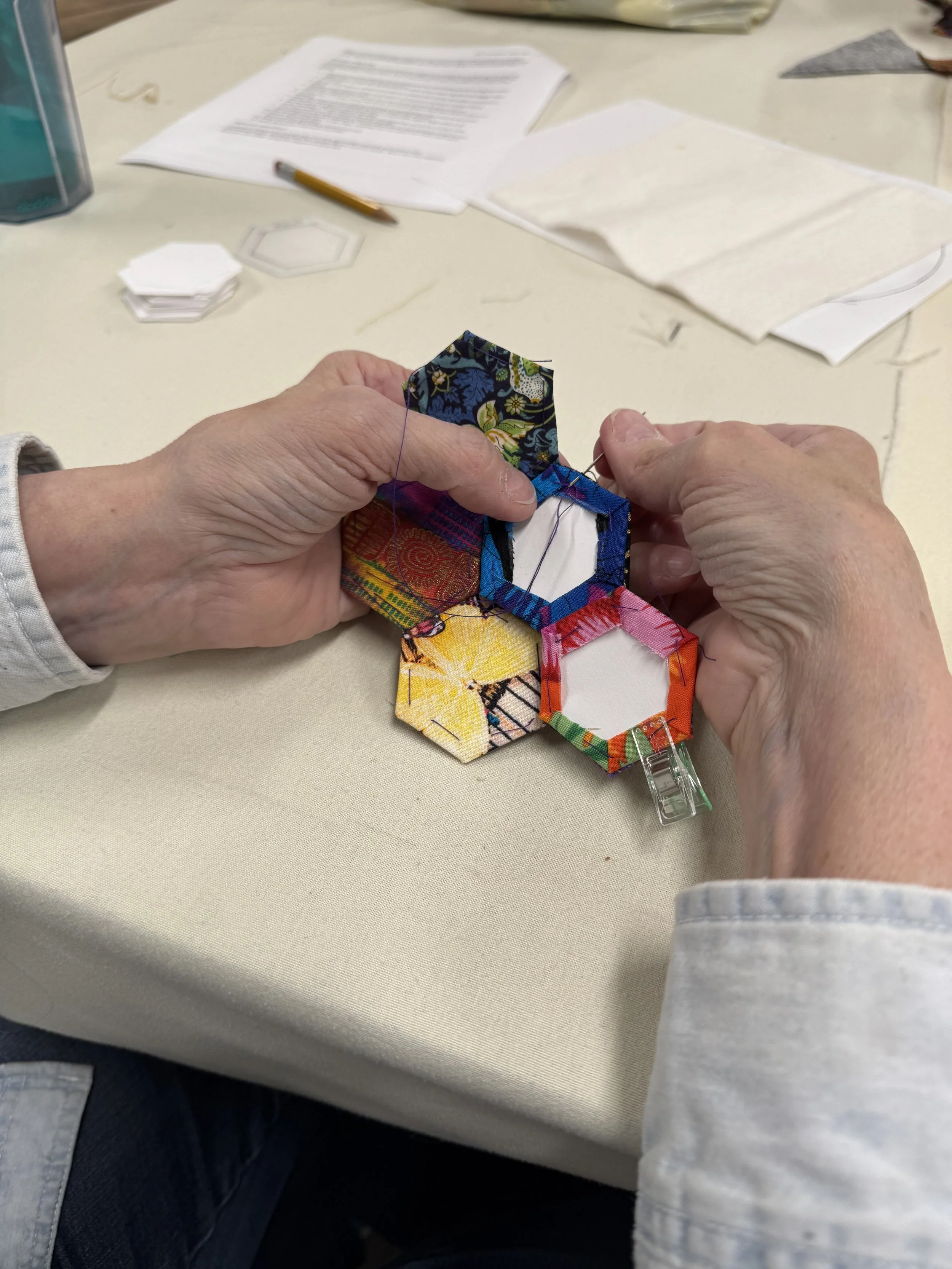 Two hands holding hexagon-shaped pieces of fabric sewn to form flower shape