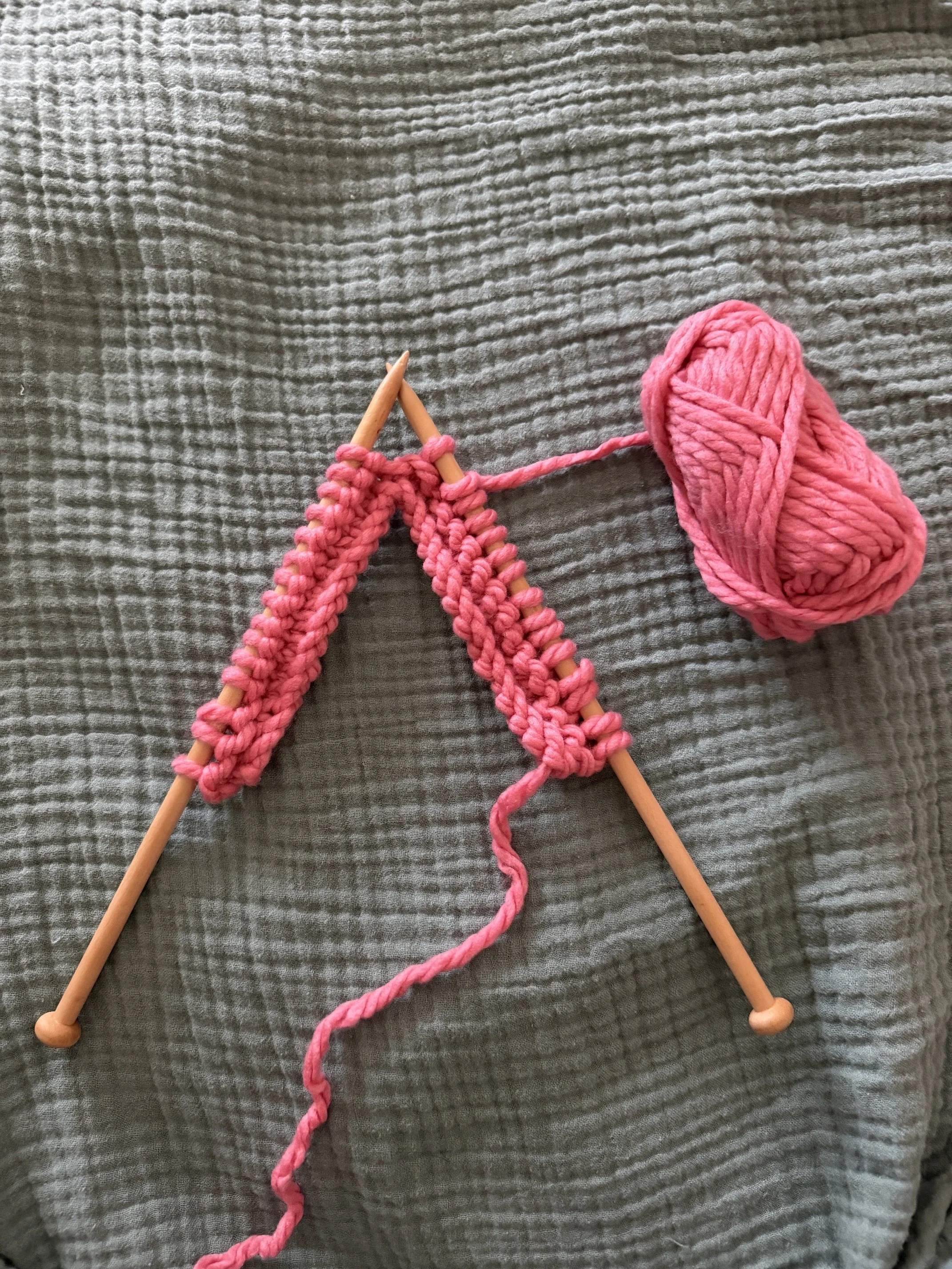 Pair of knitting needles holding knit pink yarn