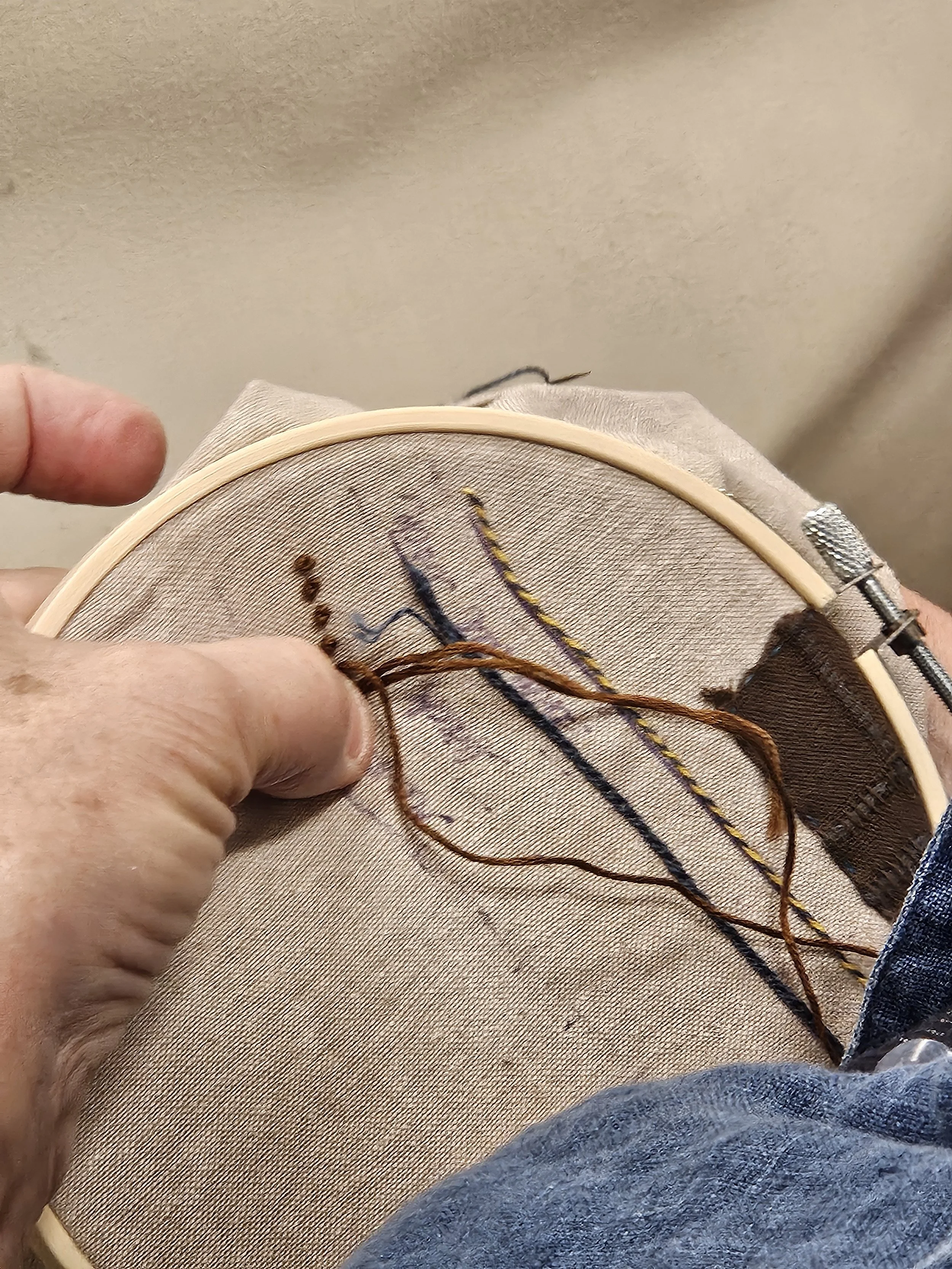 Close-up of someone holding embroidery hoop with beige fabric with brown embroidery