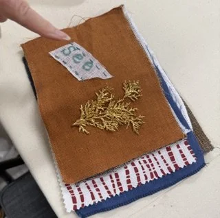 Finger pointing to brown fabric book with gold embroidered sprig and handwritten word ("See")