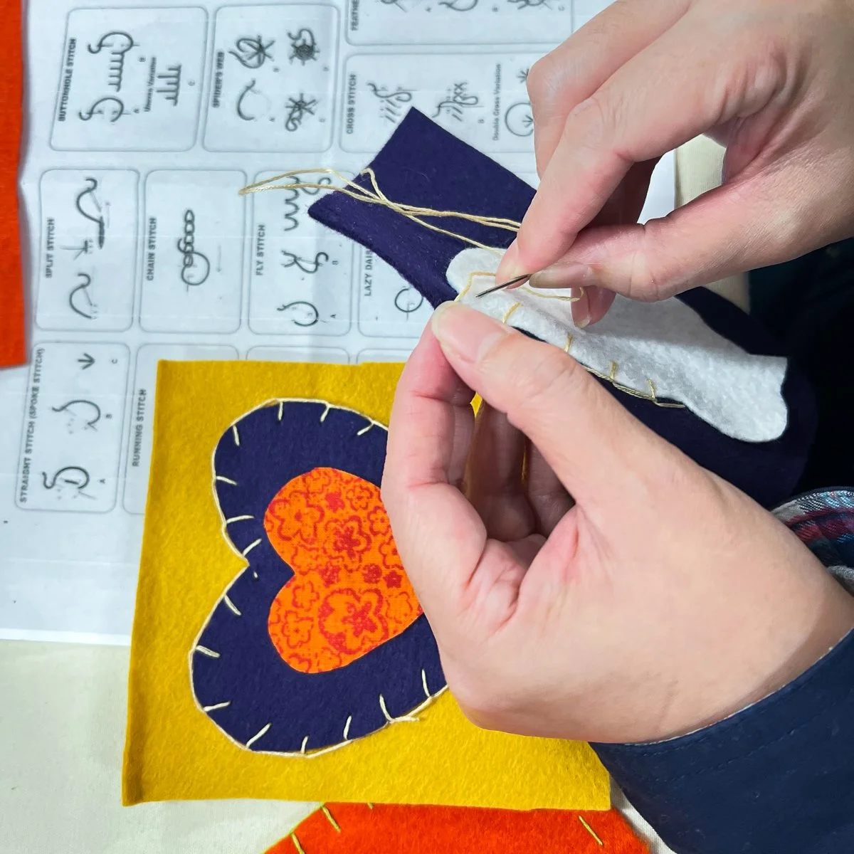 Person's hands working on sewing colorful fabric heart design