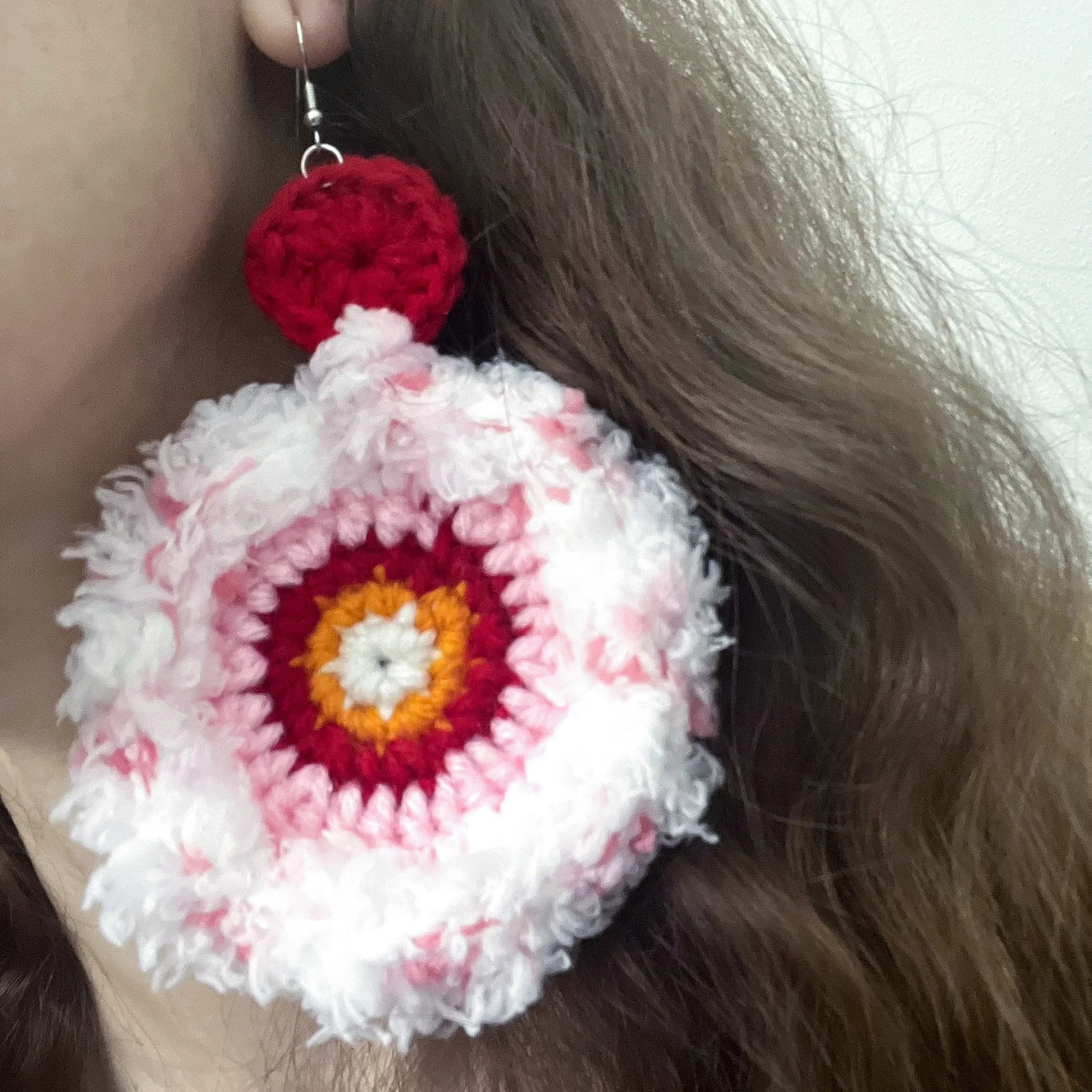 Close up of person wearing pink, red and white crocheted earring