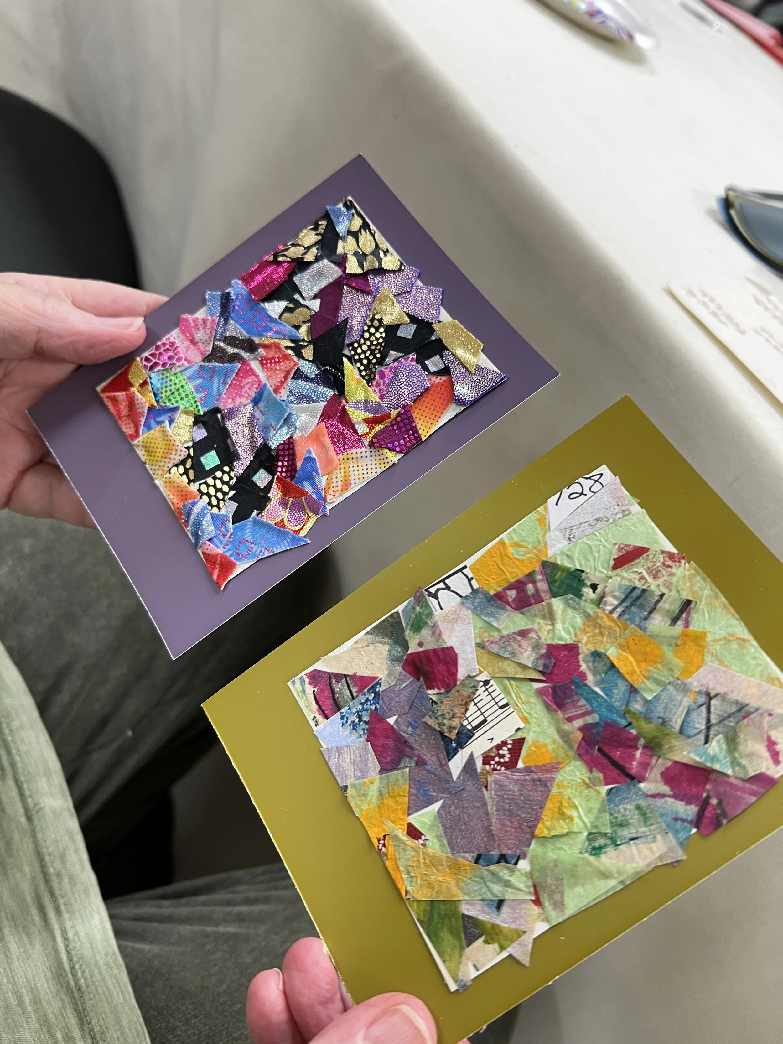 Person's hands holding up two paper collage greeting cards on purple and green paper