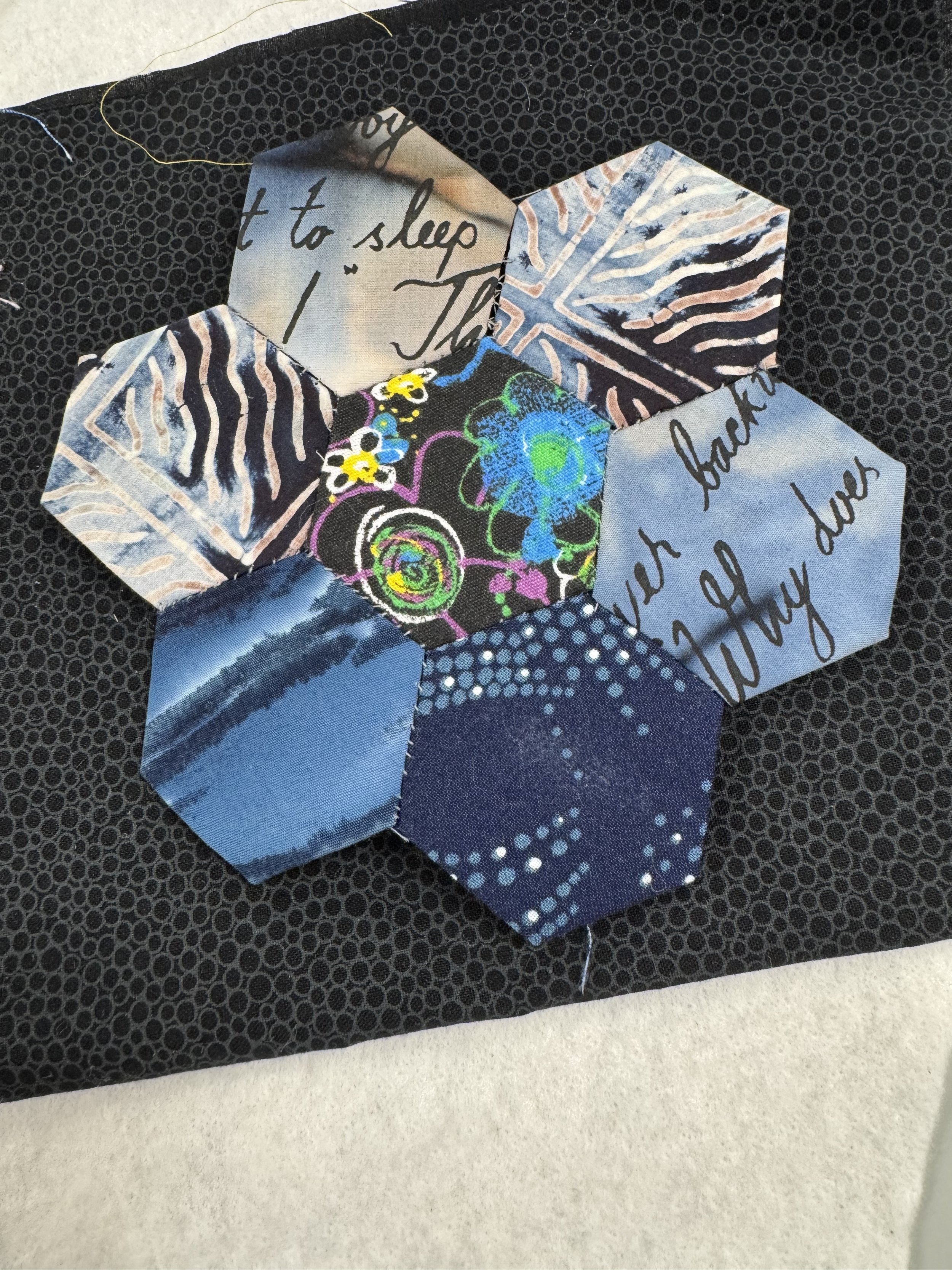 Hexagon-shaped pieces of fabric sewn to form flower shape on black background