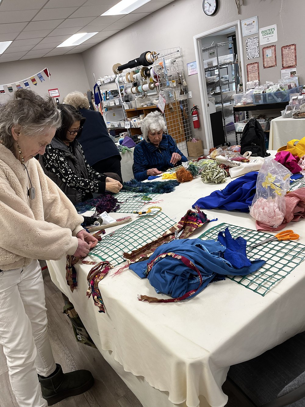 Group of women standing around table working on weaving projects