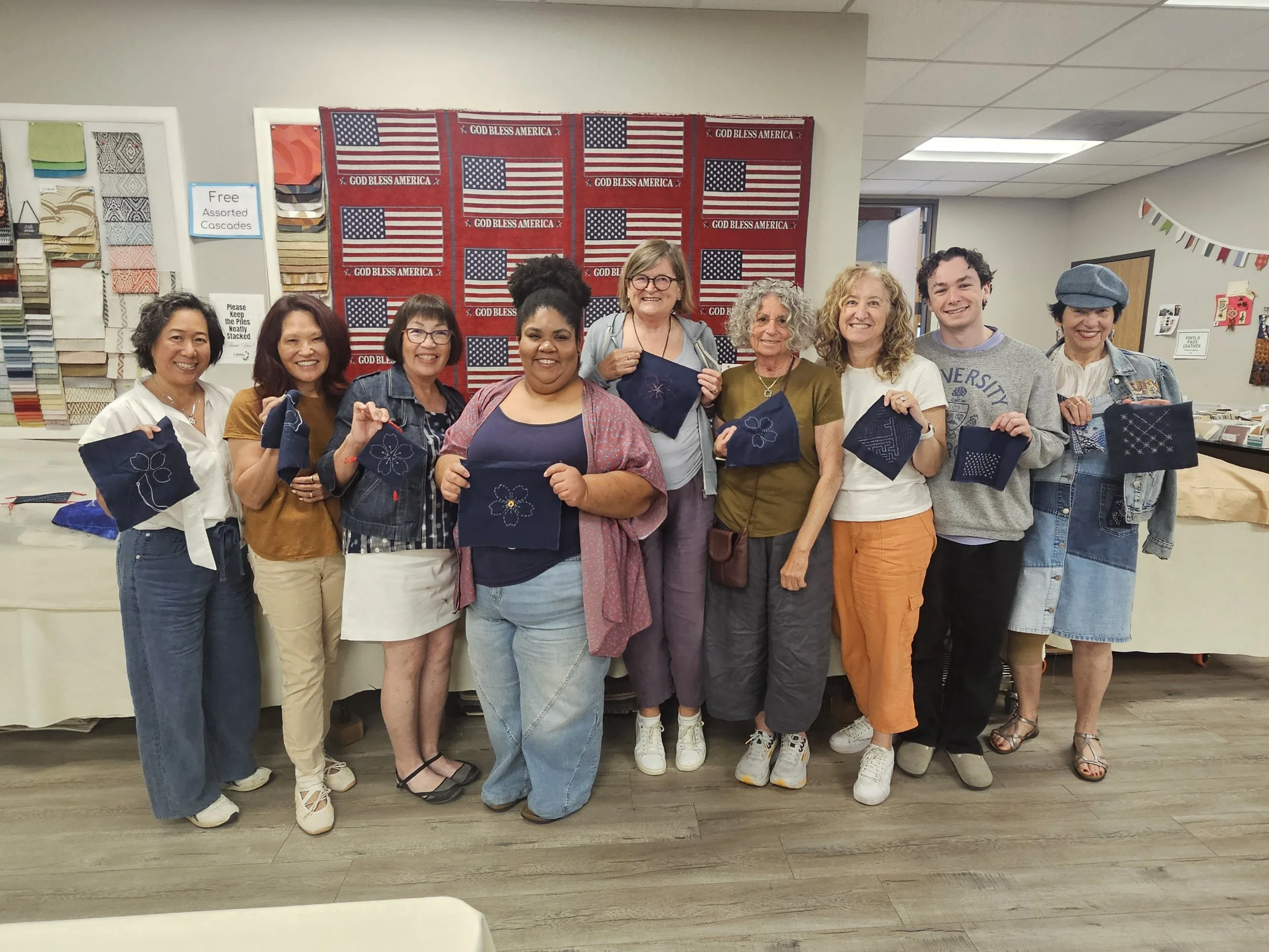Group of nine smiling people holding up sashiko embroidered on dark blue fabric squares