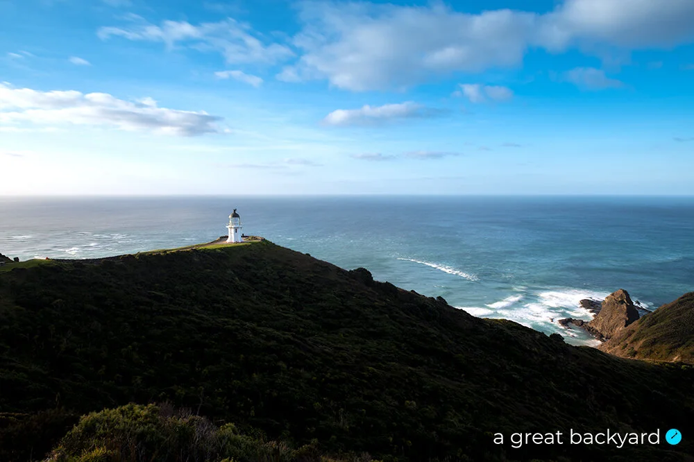 View across hill to Cape Reinga lighthouse and blue Pacific Ocean beyond