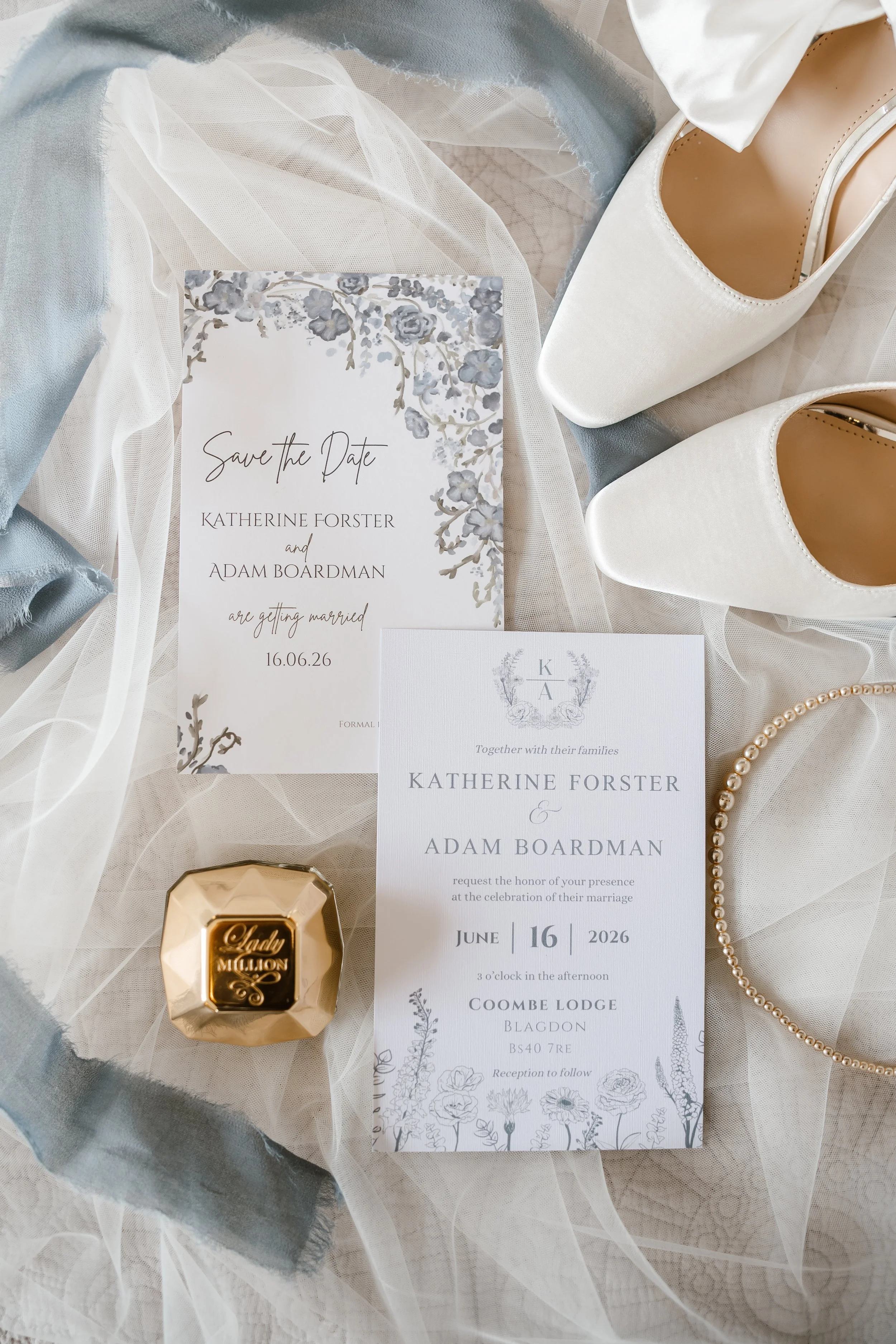Wedding invitation cards, a pair of white high-heeled shoes, a pearl necklace, a gold hexagonal box with 'Lady Million' written on it, and a string of pearls, all arranged on a soft fabric background.